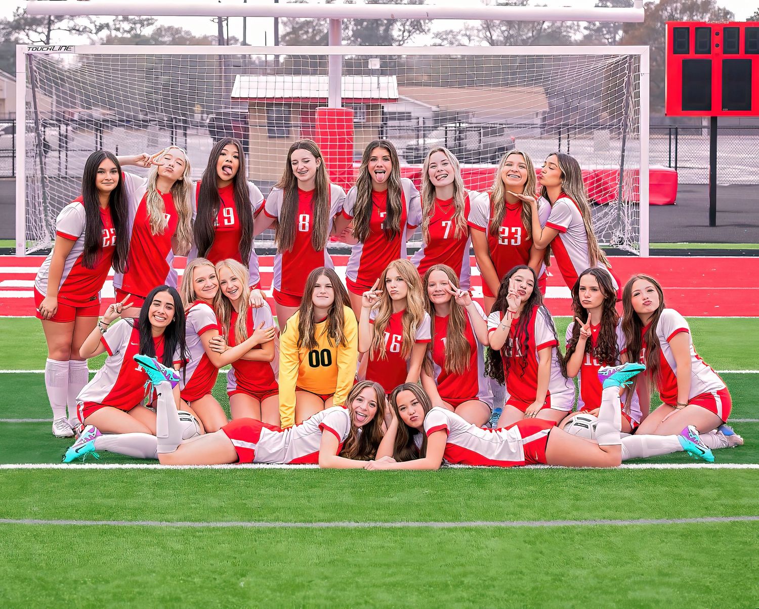 High school girls soccer team poses together in red uniforms on green turf field for team photos.