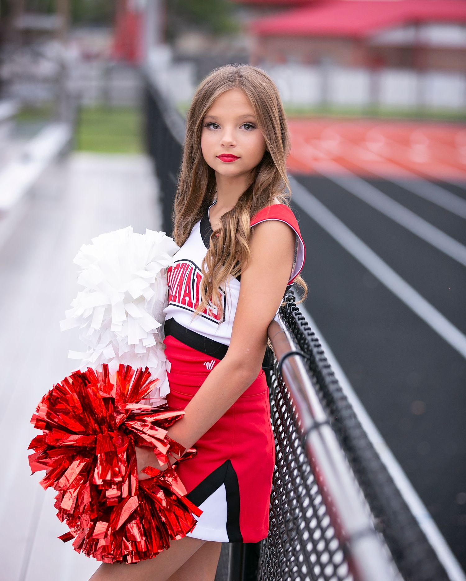 Cheerleader in red and white uniform poses with pom poms on a football field during a photo session.