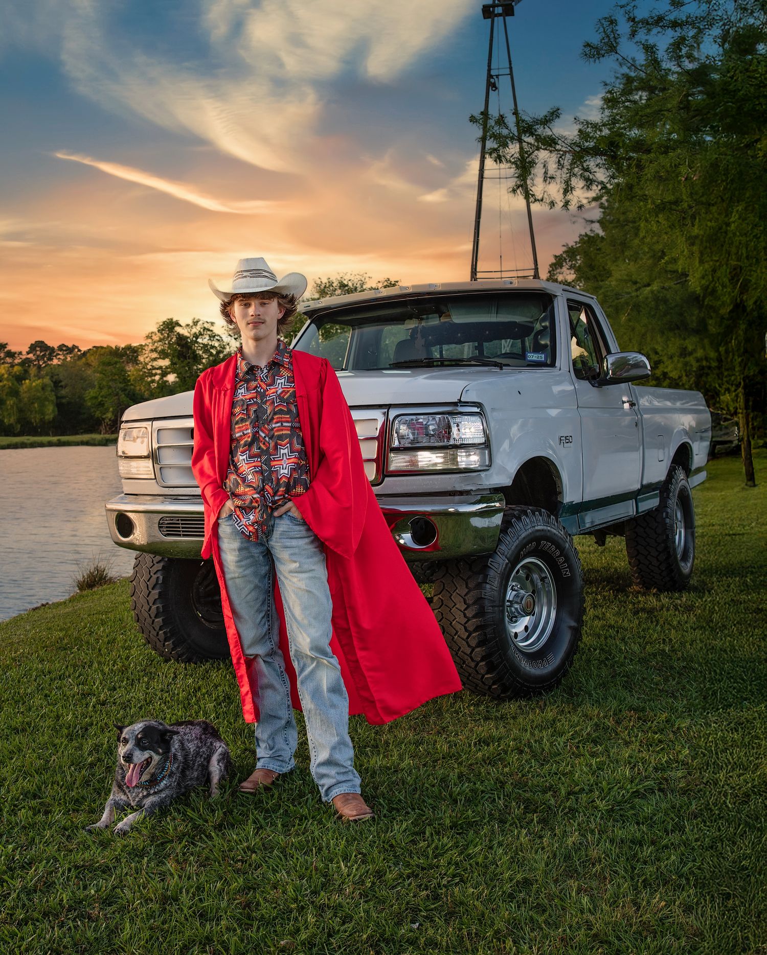 Person in red coat and cowboy hat poses with white lifted truck and dog at sunset.