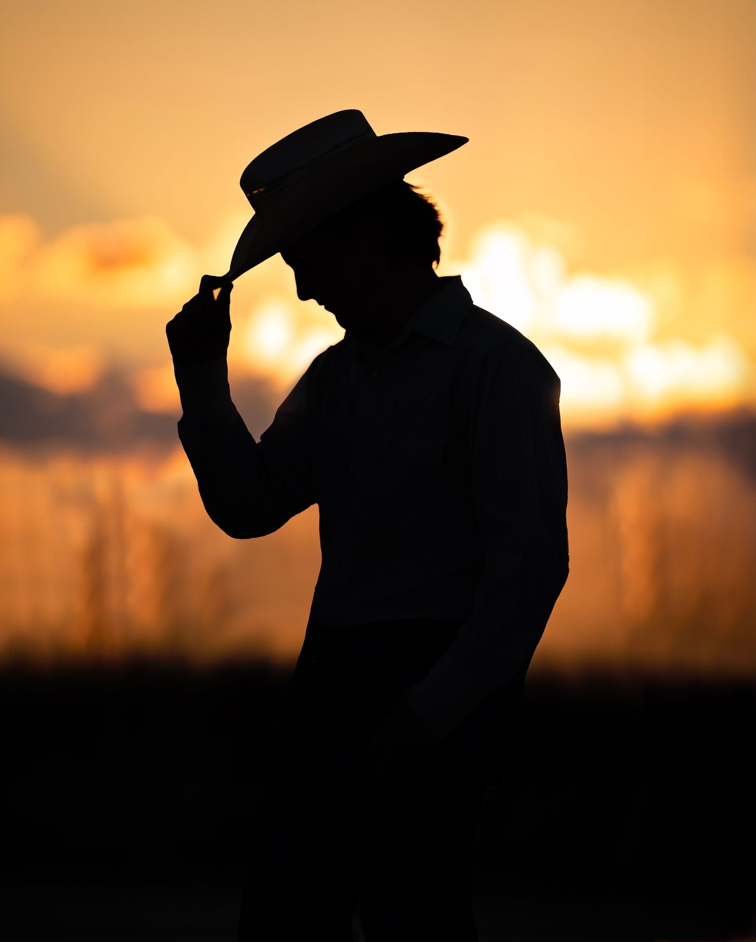 Silhouette of a cowboy tipping his hat against a golden sunset sky.