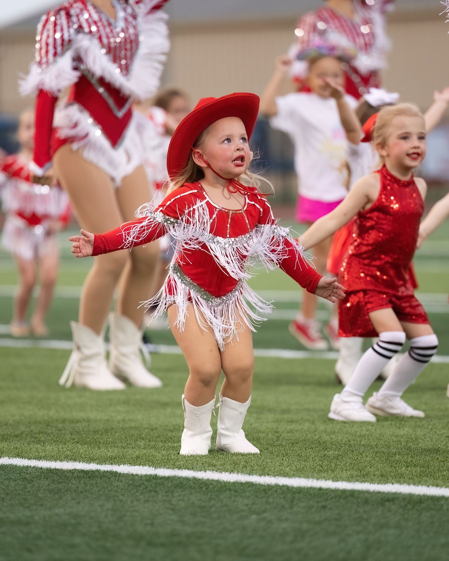 Cheerleaders in red and white uniforms perform a synchronized dance routine on a football field.