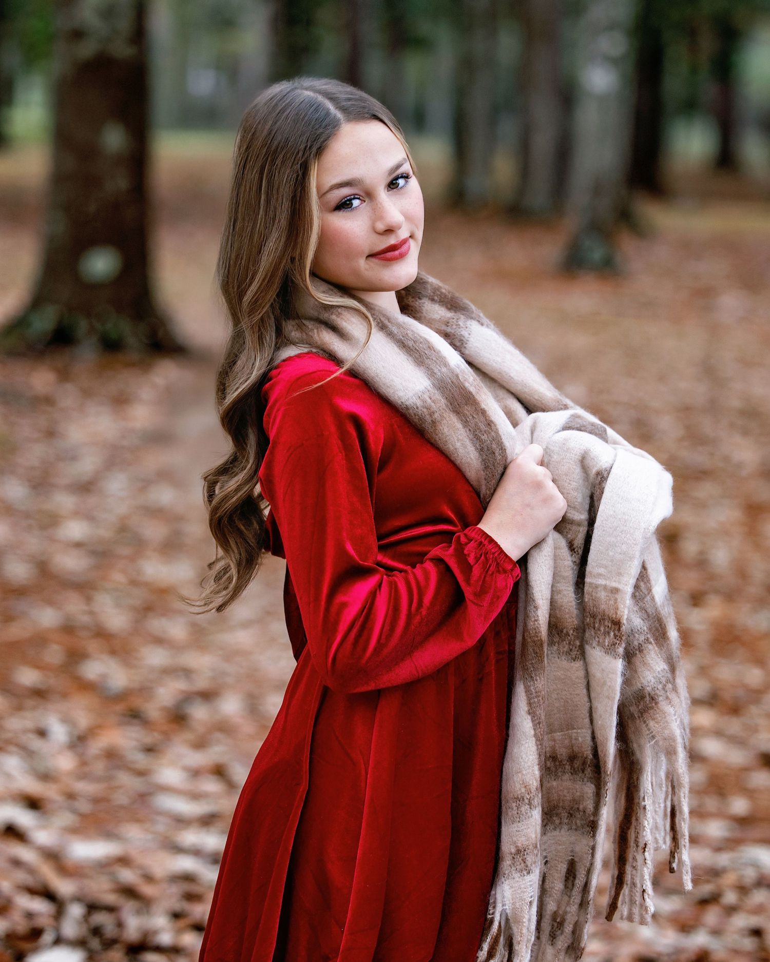 Autumn fashion portrait featuring red velvet dress and plaid scarf among fallen leaves.