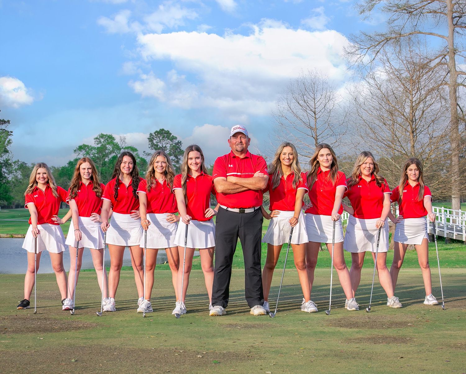 Group of performers in matching red and white outfits stand together in a line outdoors on a sunny day.