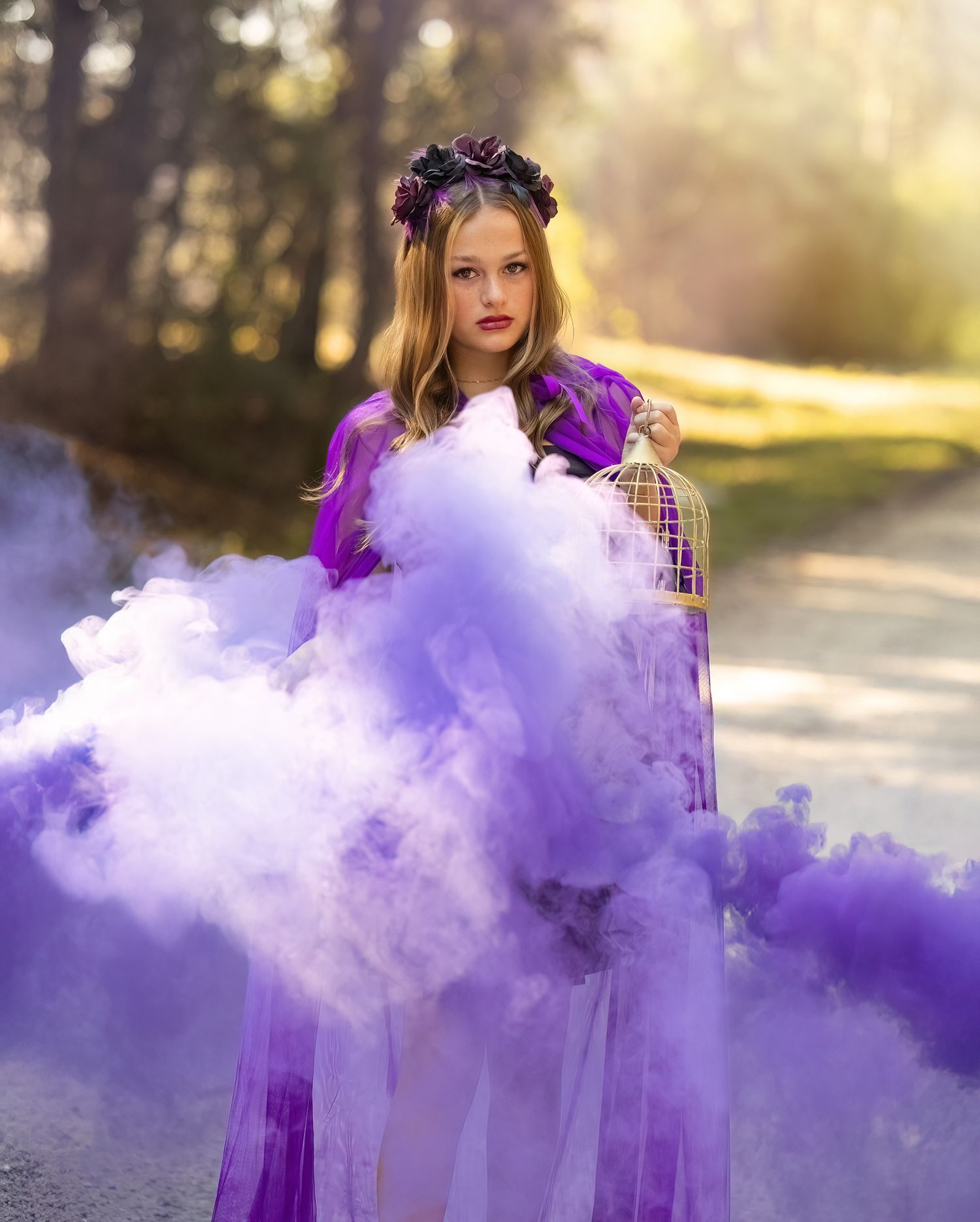 Ethereal portrait with flowing purple smoke effects in a sunlit forest path.