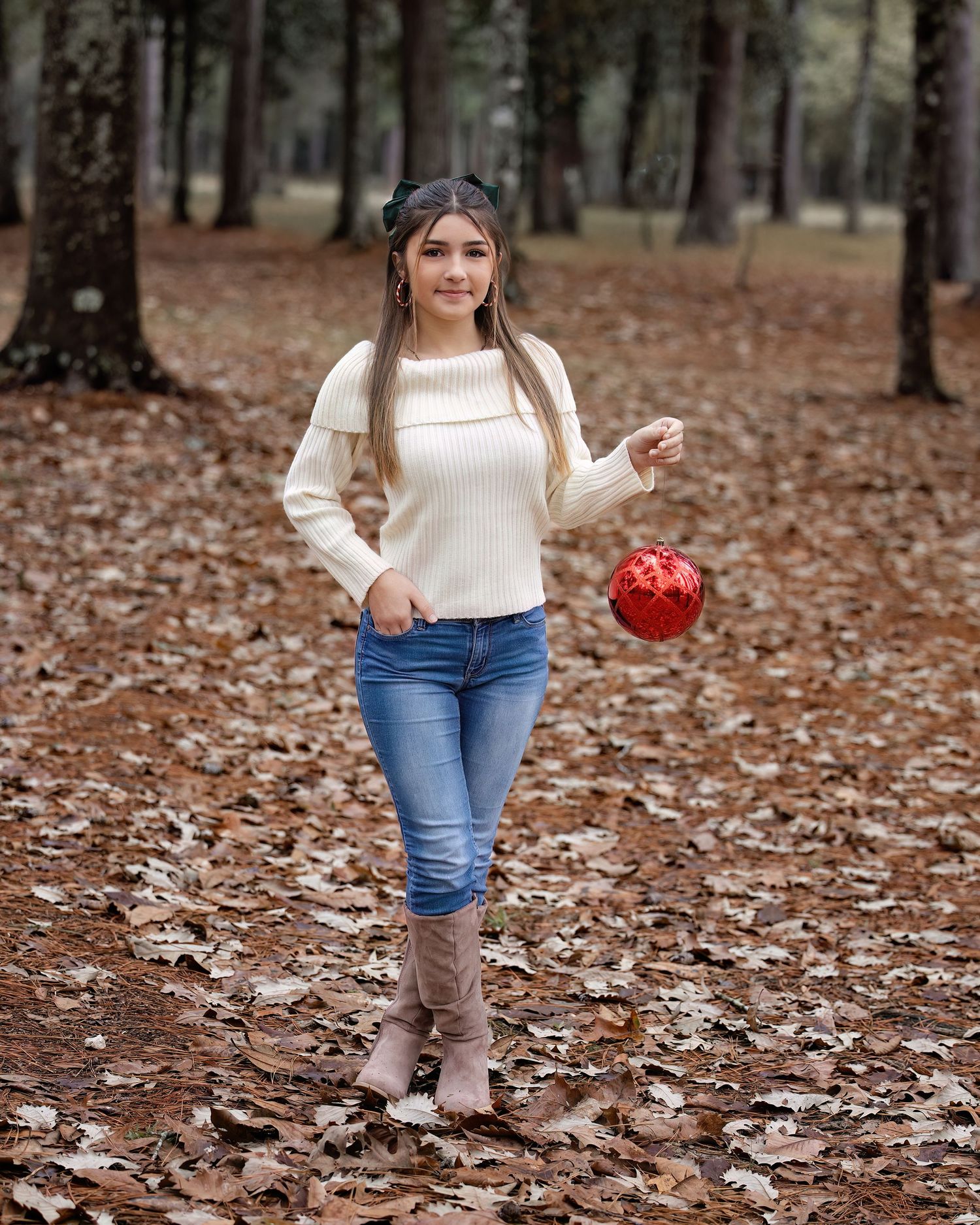 Casual winter outfit featuring cream sweater, jeans and boots photographed in park with fallen leaves.