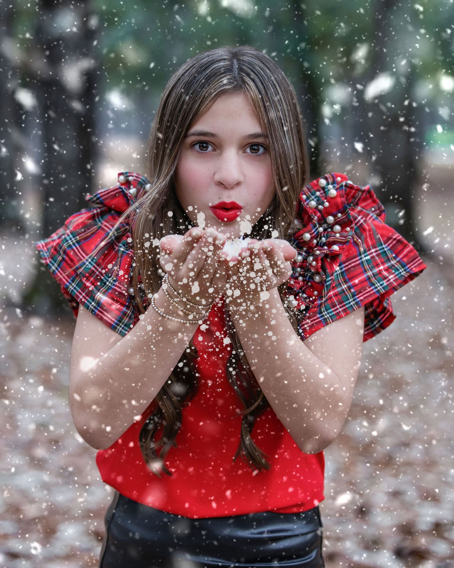 A winter photoshoot with falling snow and someone wearing plaid and red blowing sparkles.
