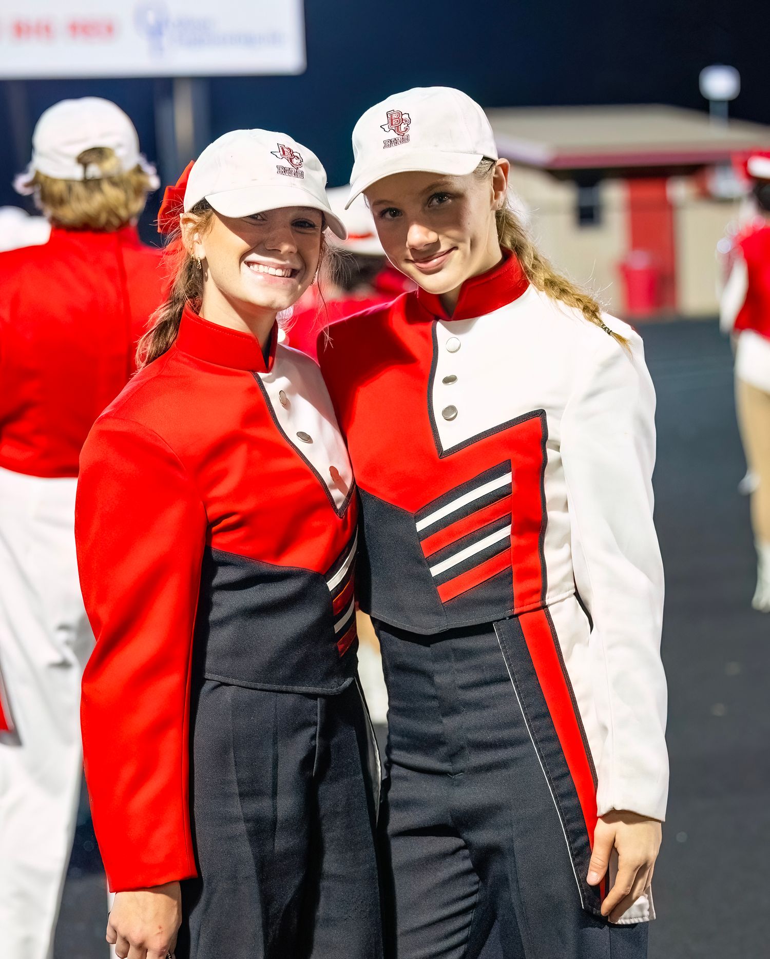 Two band members in red and white uniforms with matching baseball caps pose together at a performance event.