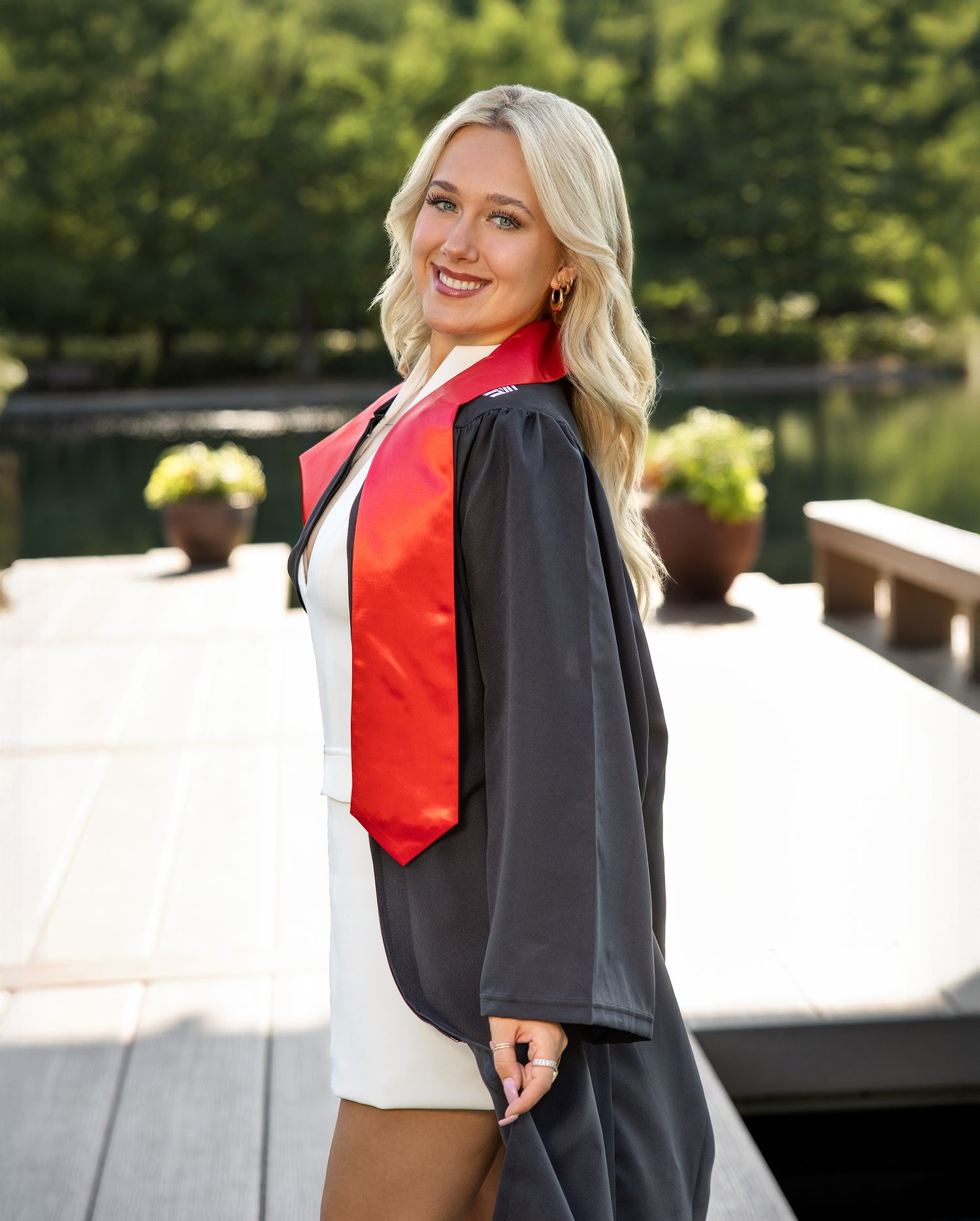 A figure in a navy blazer and red scarf poses outdoors against a white wall.