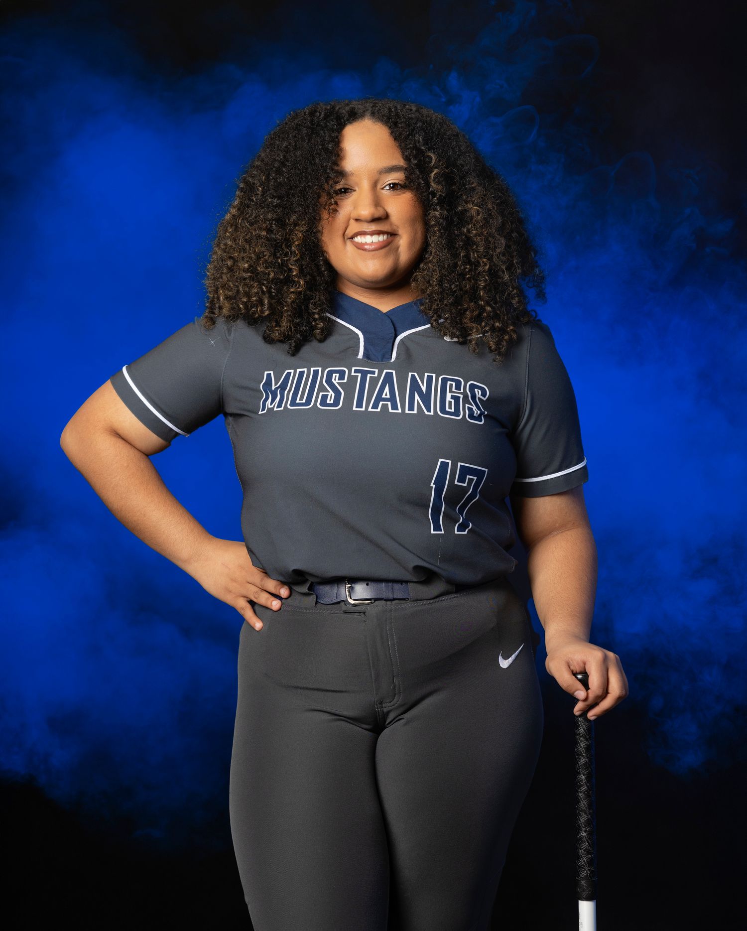 High school softball player poses in Mustangs team uniform against dramatic blue backdrop.