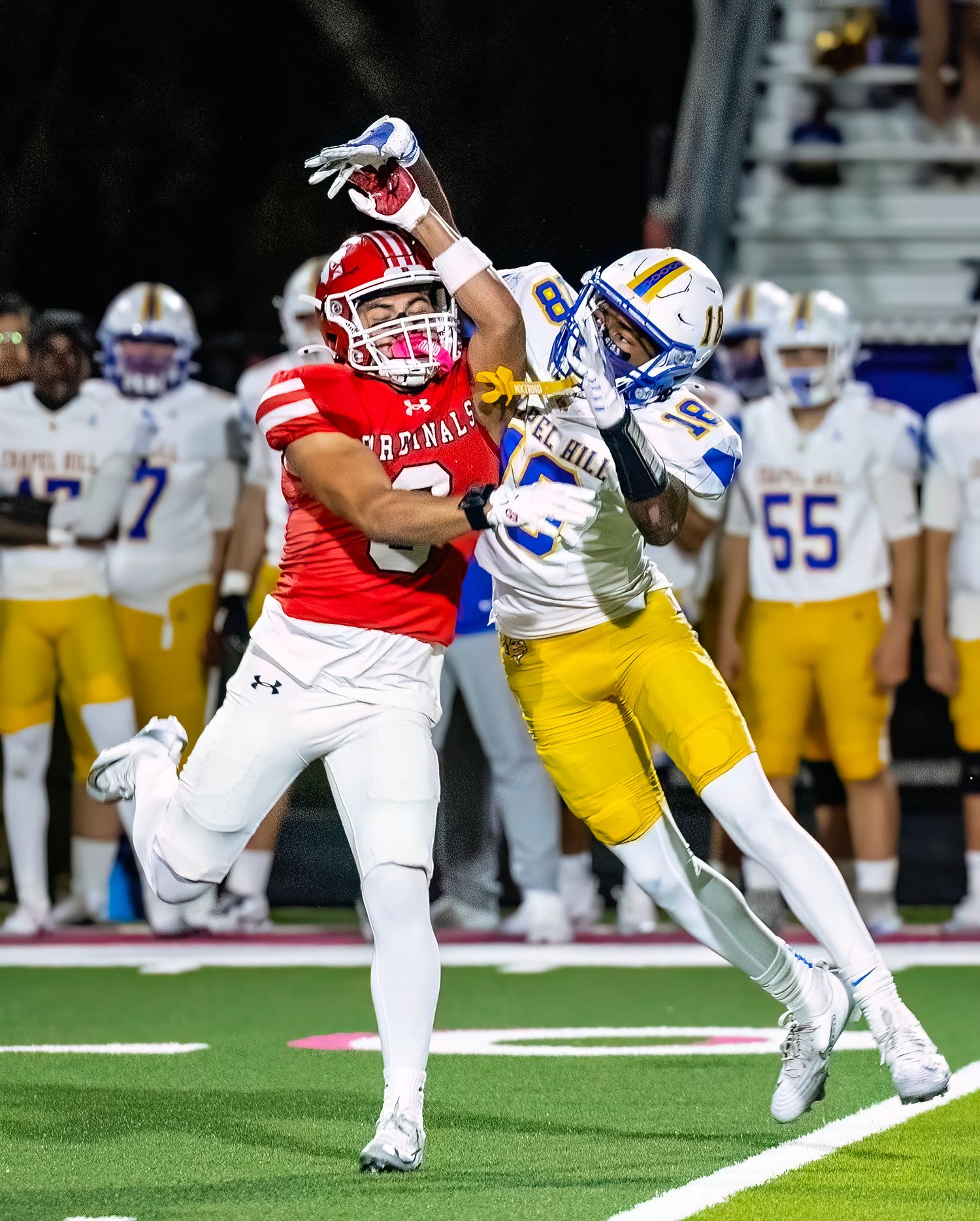 Football players in red and white uniforms tackle an opponent in yellow during an intense game play.