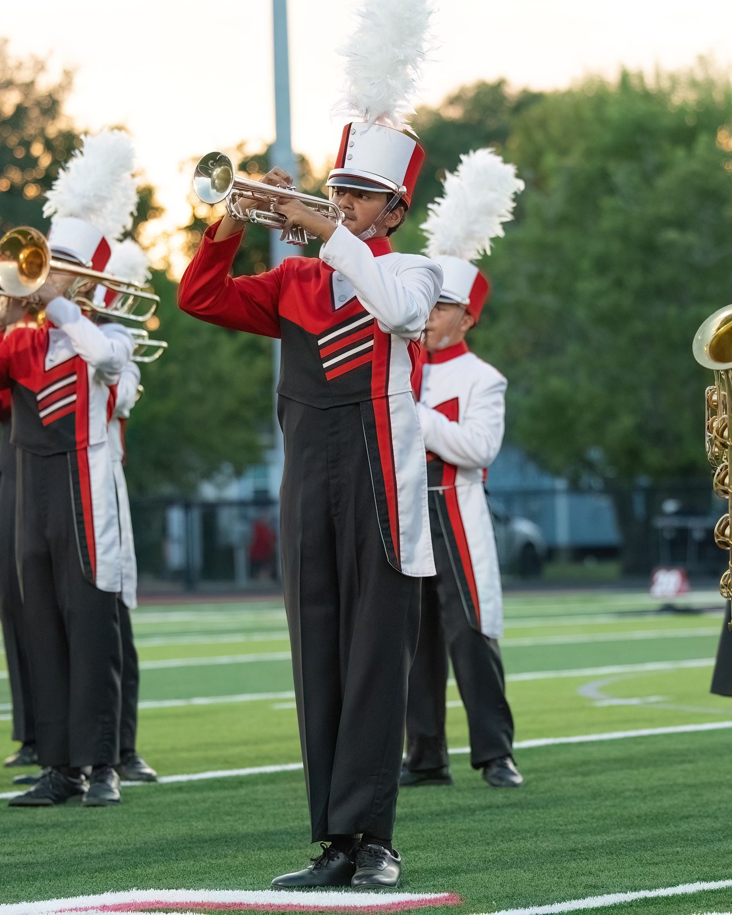 Marching band members in black uniforms perform with instruments on the football field.