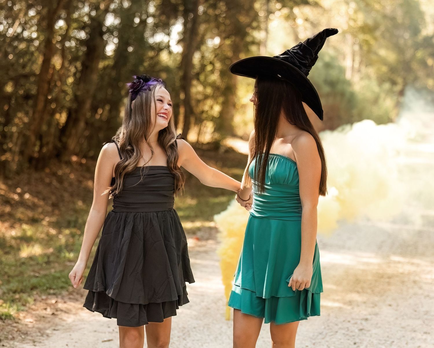 Two friends in dresses laugh together on path with one wearing witch hat.