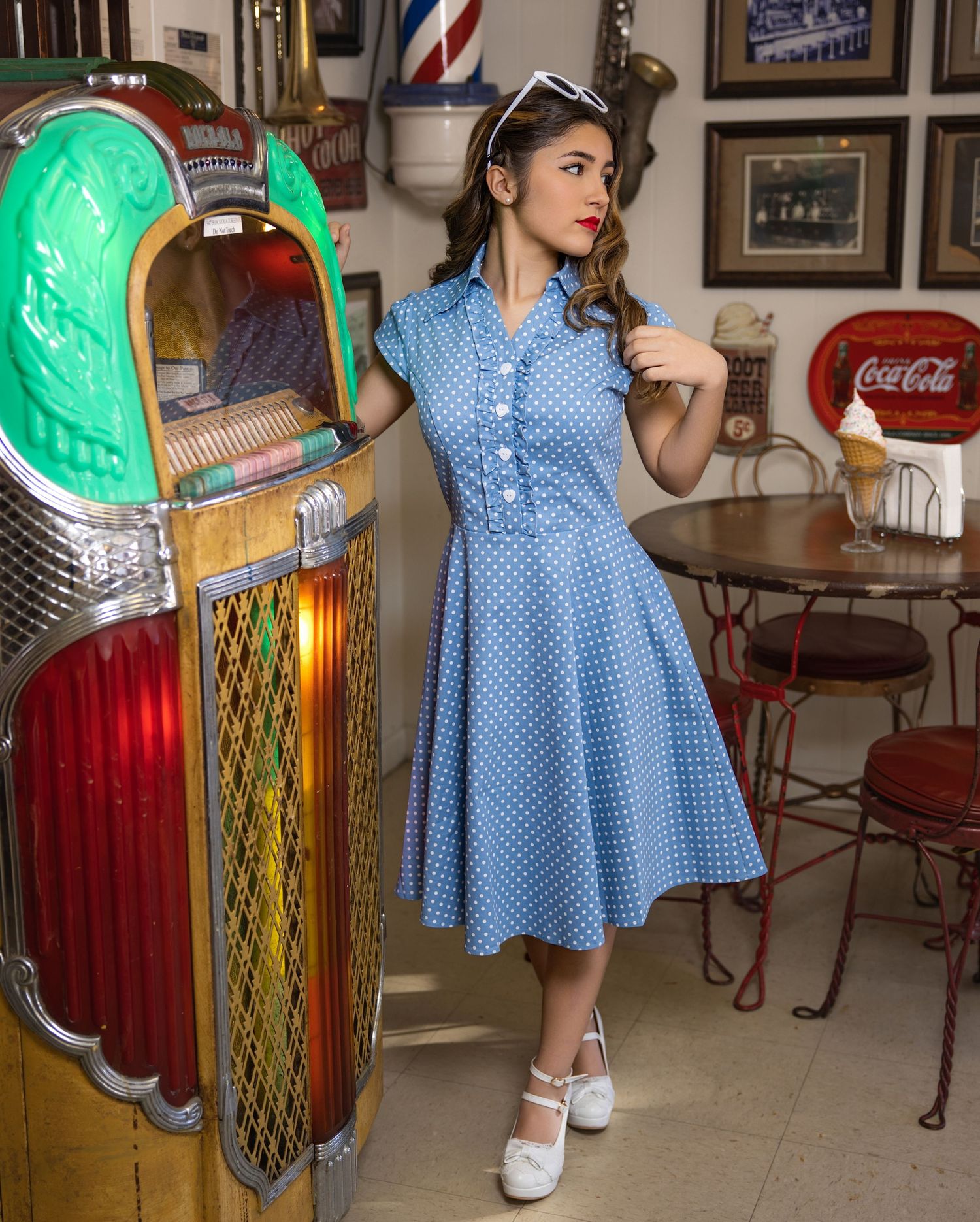 A retro-styled scene showing someone in a polka dot dress and white shoes standing in a vintage diner setting.