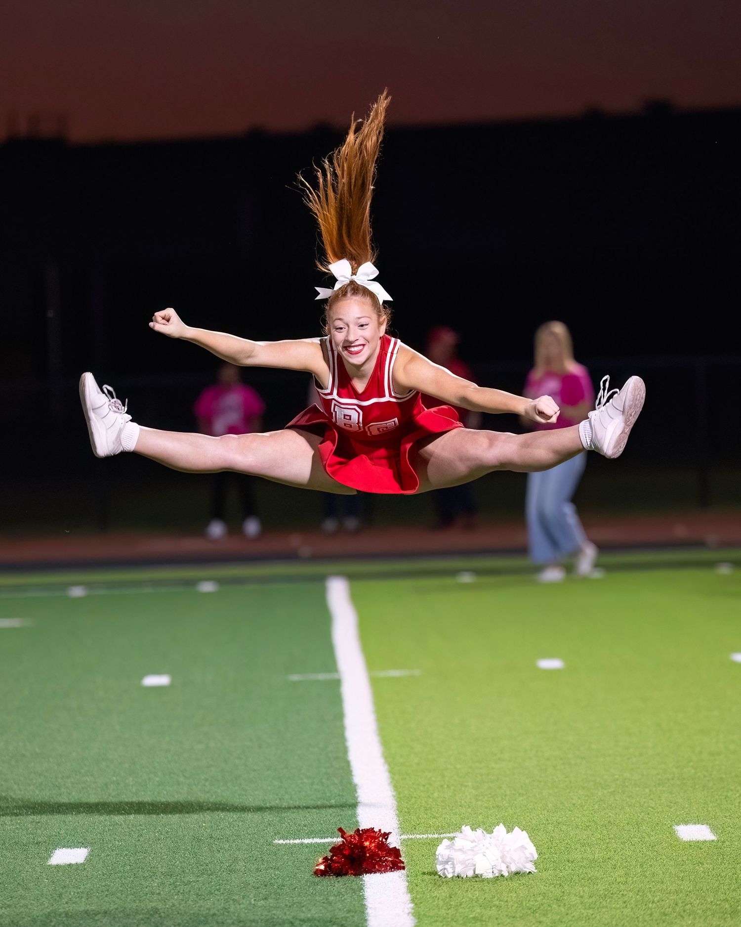 Cheerleader performs an impressive aerial split jump sequence on a football field at night.