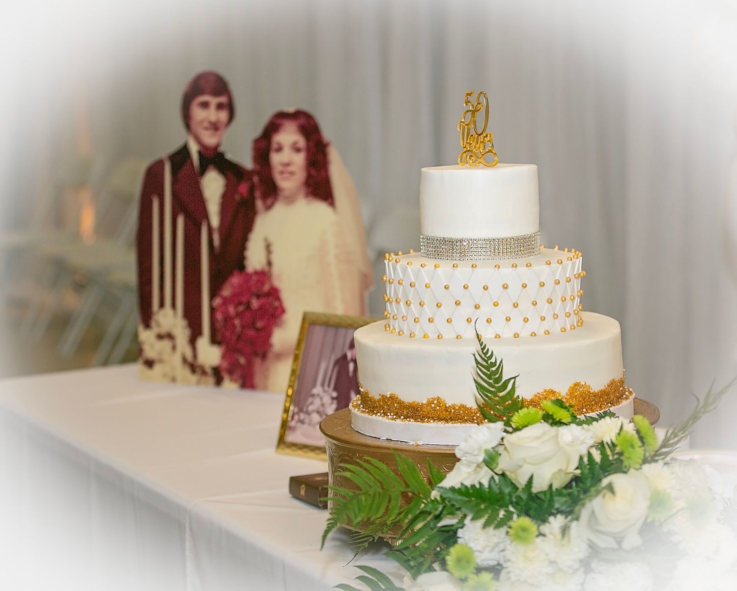 A multi-tiered white wedding cake decorated with delicate gold dots and fresh green ferns on display.