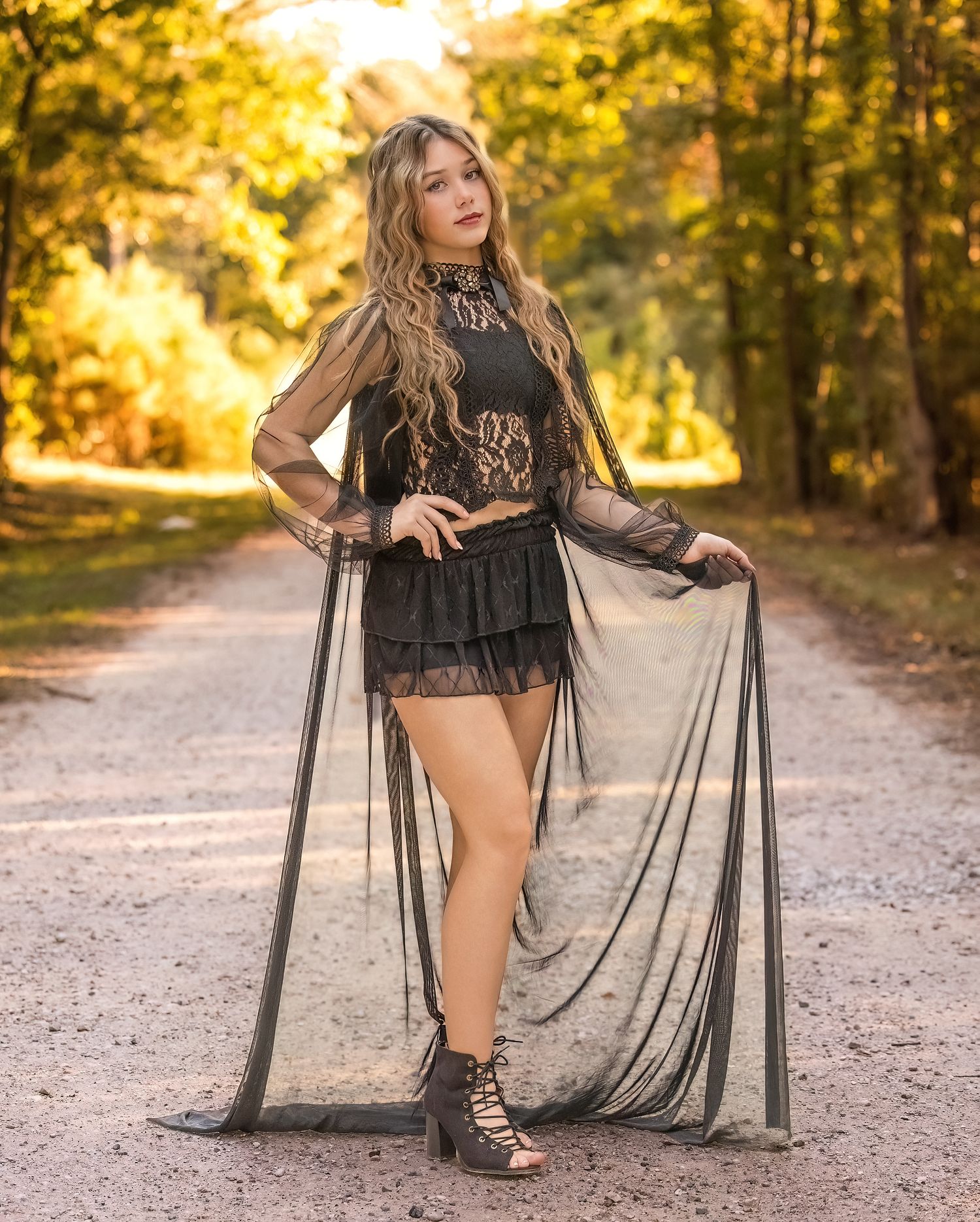 An outdoor portrait session showing someone in a black flowing dress on a sunlit gravel path.