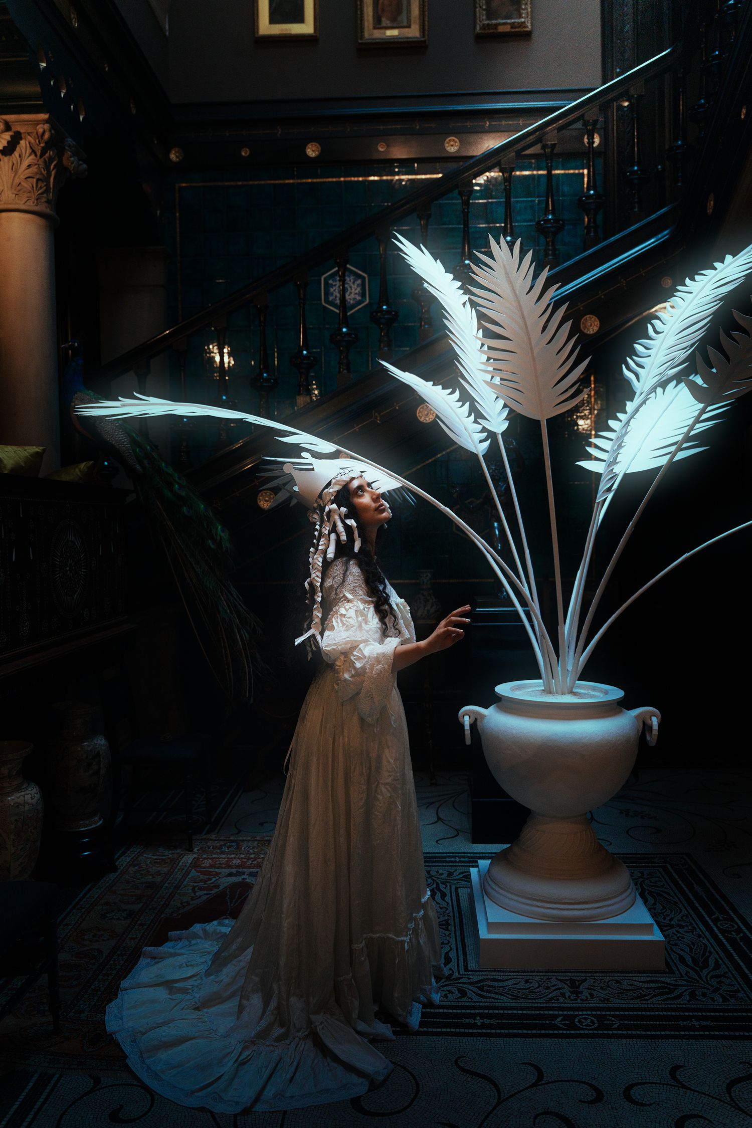 Woman in white lace gown reaching toward glowing illuminated palm fronds in dark interior.