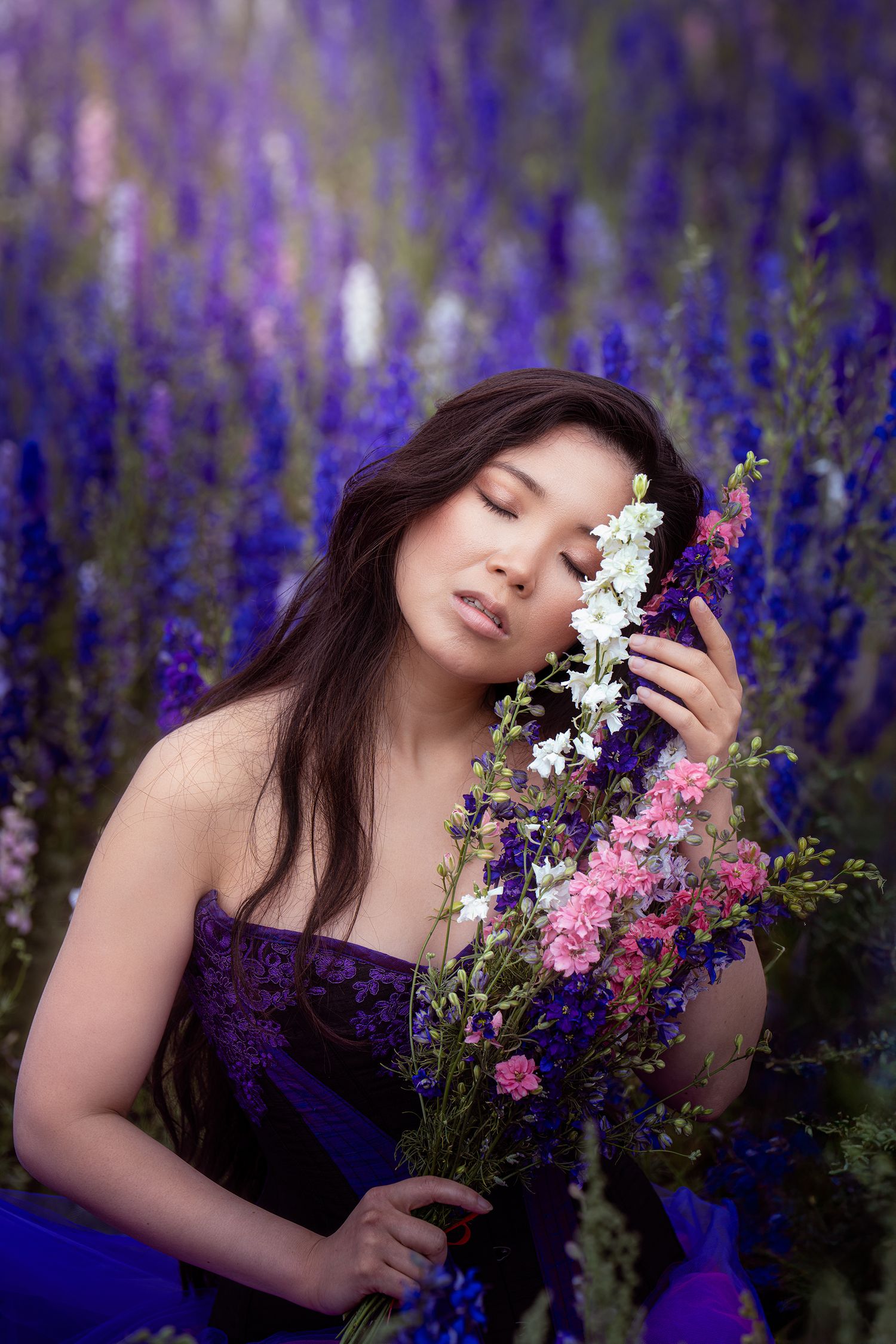 Serene Asian woman with closed eyes holding wildflowers in a vibrant purple lavender field.