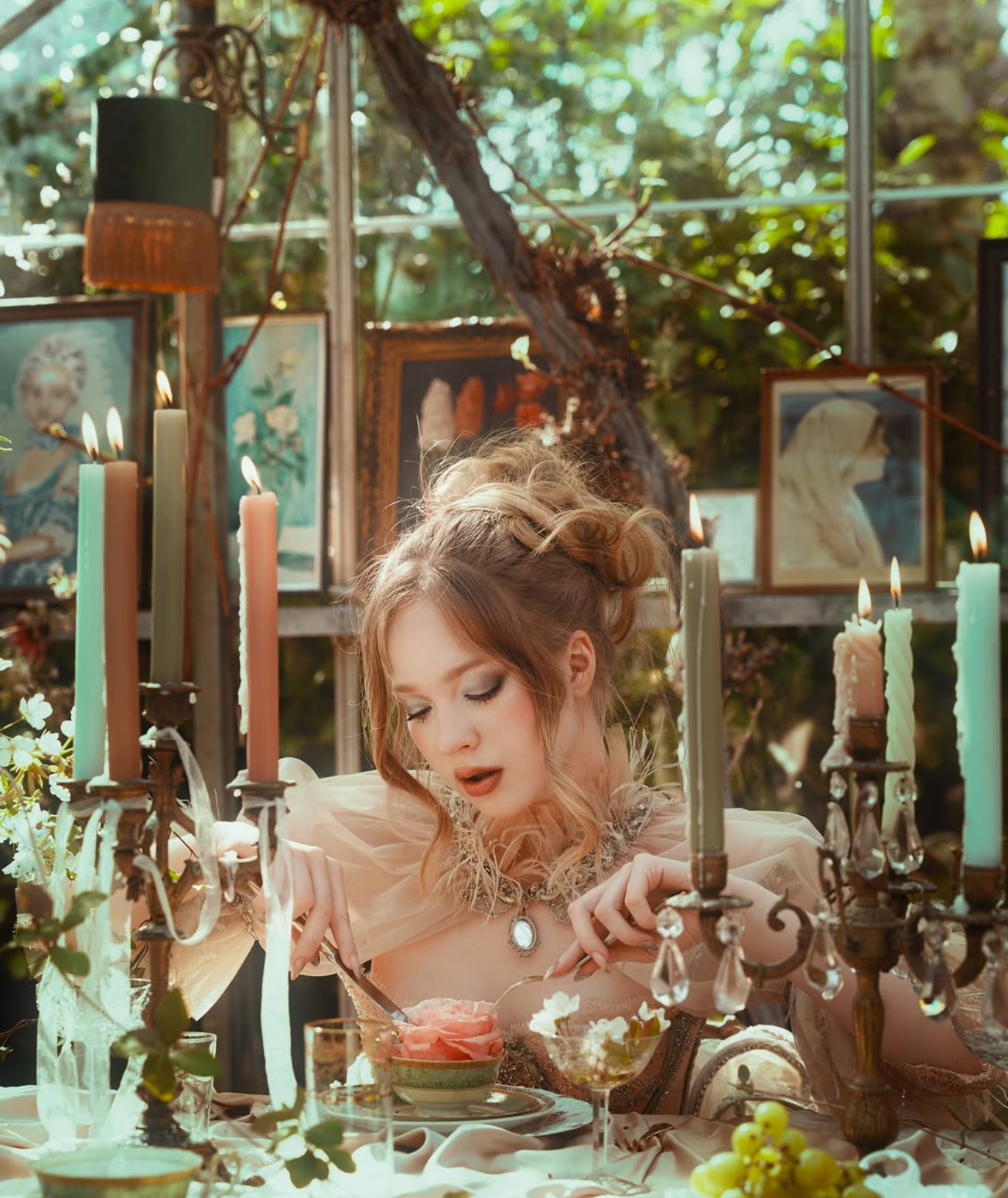An elegant woman in a vintage gown sits at a candlelit table surrounded by artwork and lush greenery.
