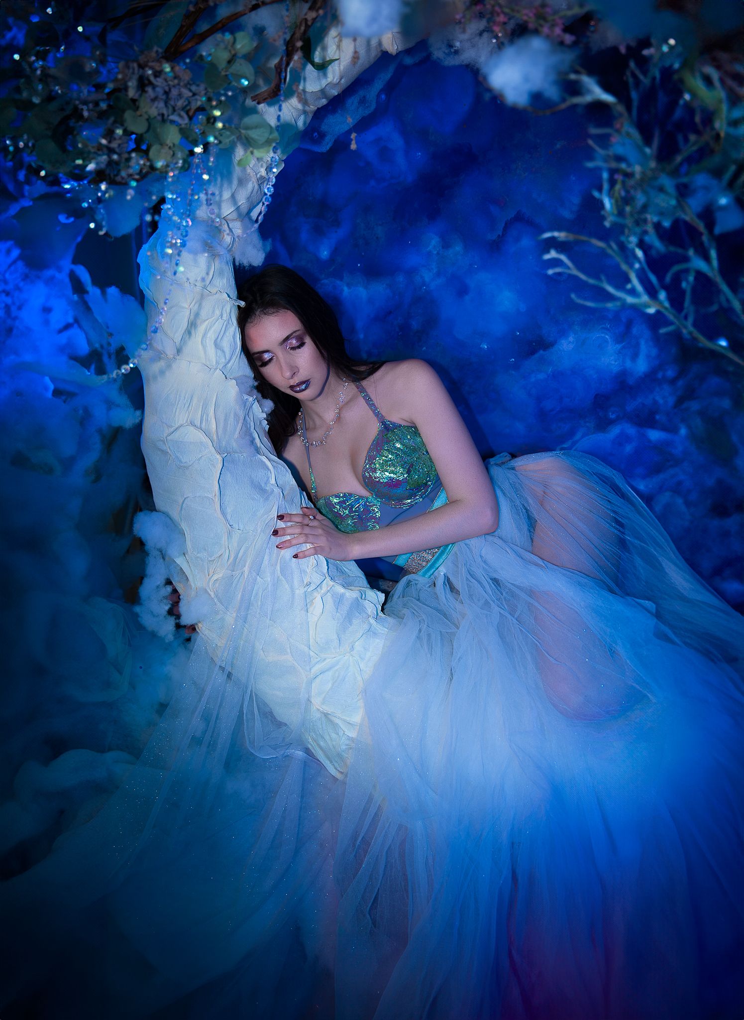 Mysterious woman in sequin top and blue tulle skirt surrounded by dramatic blue smoke.