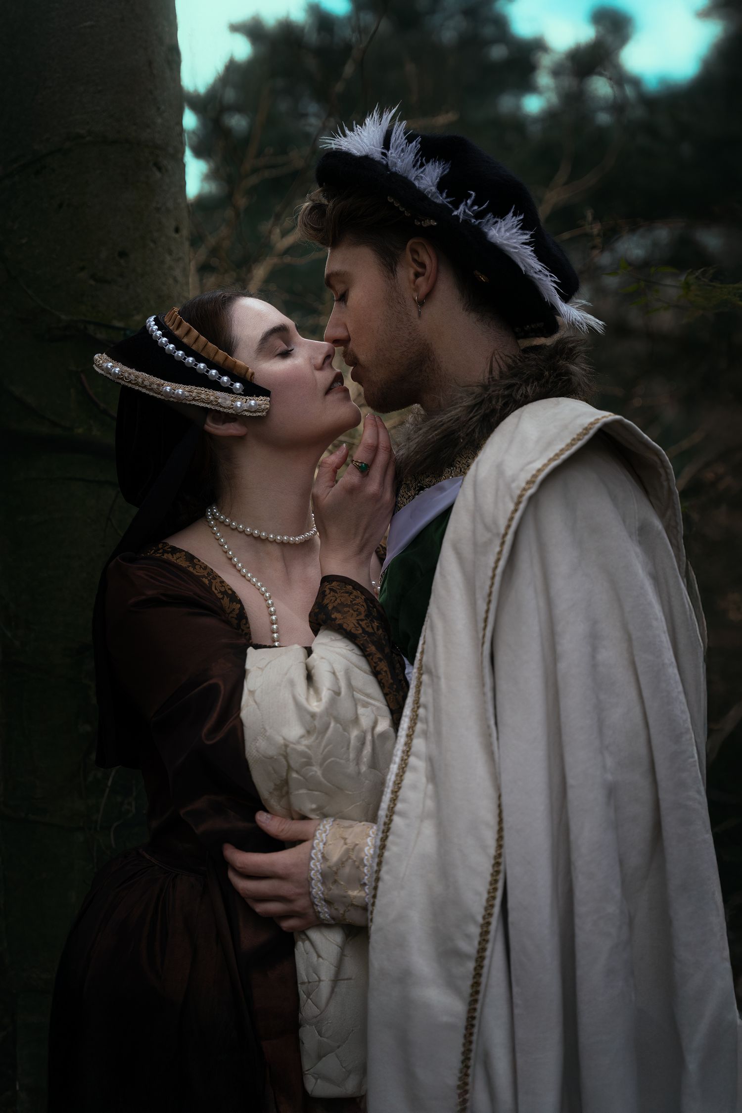 Medieval couple in historical costumes sharing a romantic moment in a dark enchanted forest setting.