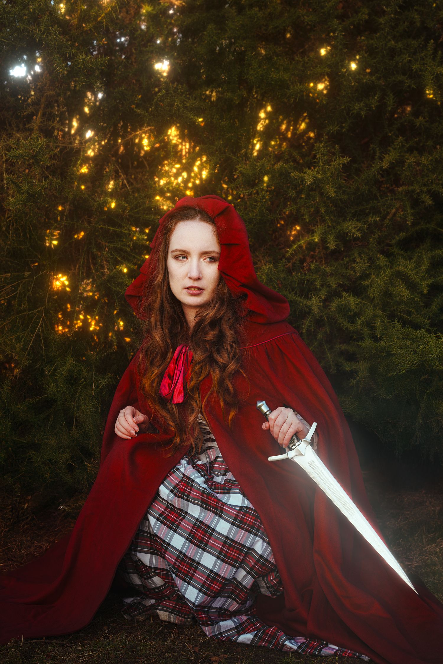 Woman in red hooded cloak wielding a glowing sword in an enchanted forest.