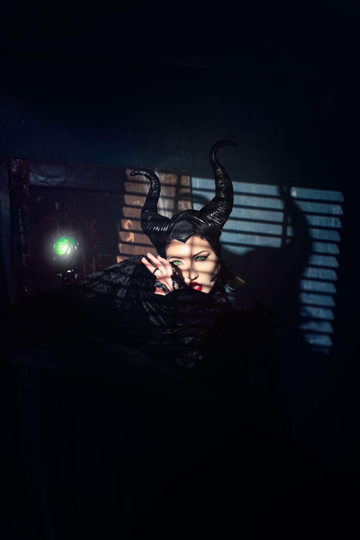A woman dressed as Maleficent with dramatic black horns poses mysteriously in a dark moody setting.