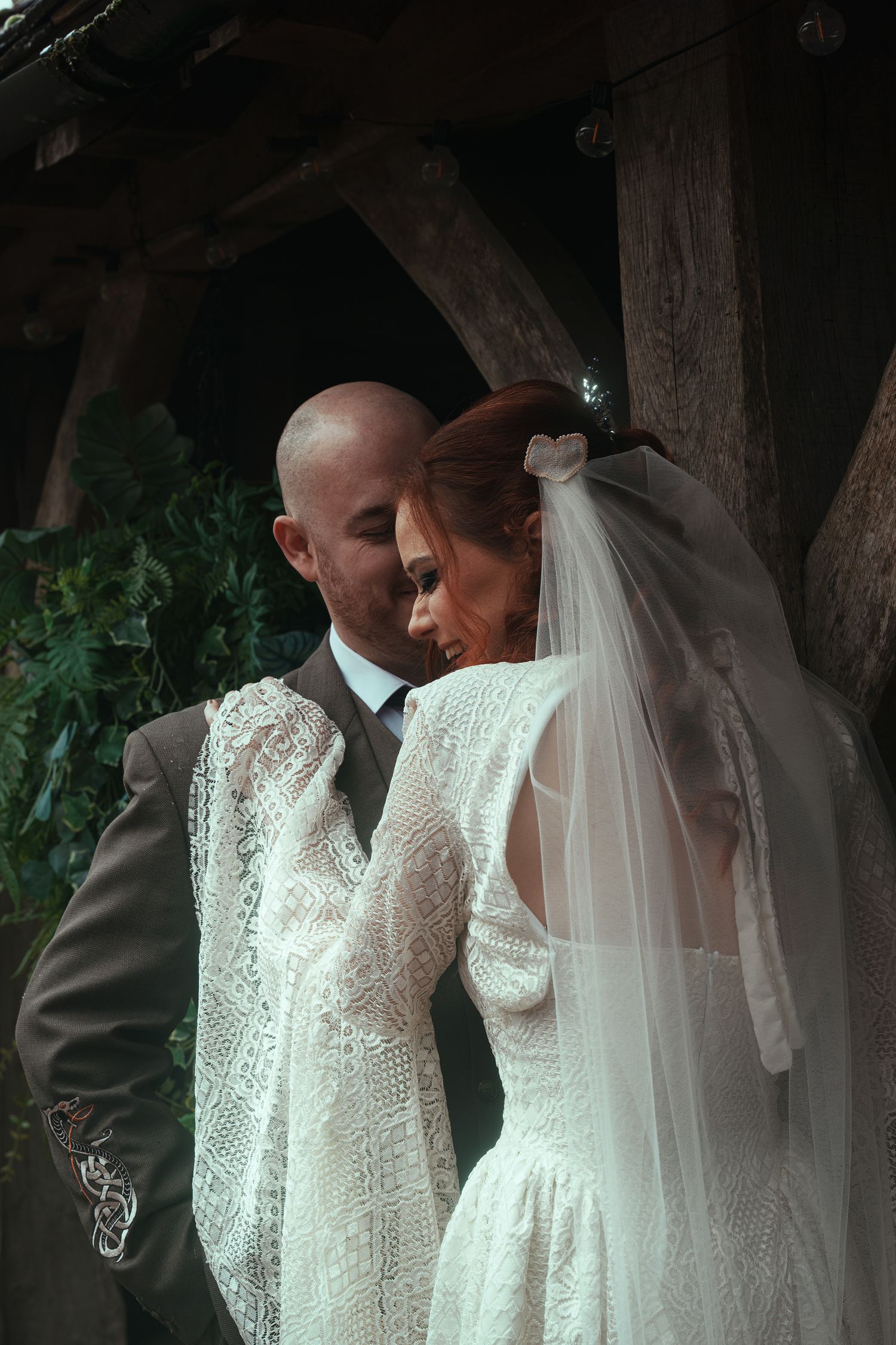 A bride in a lace long-sleeve gown and veil shares an intimate moment with her groom outdoors.