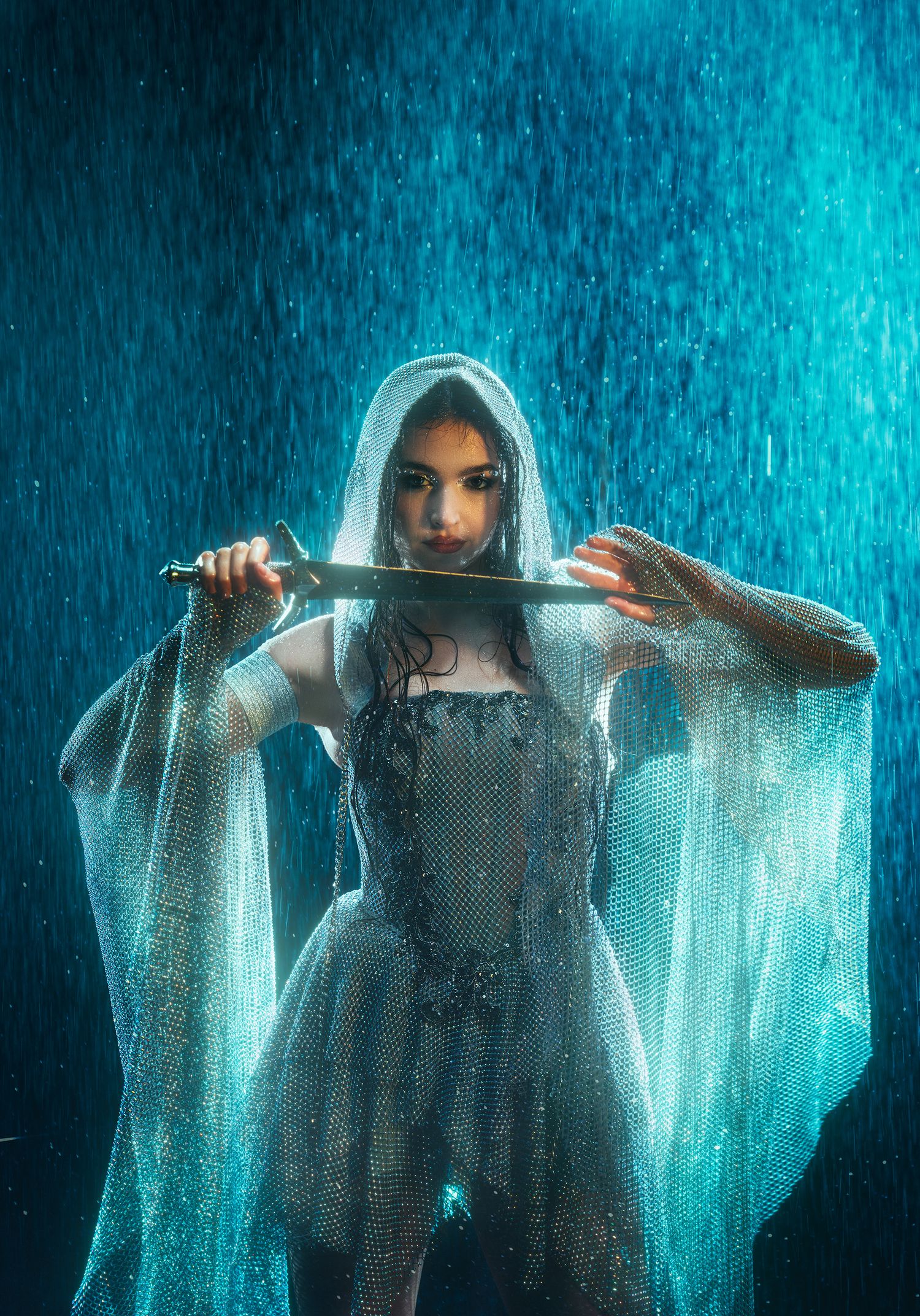 Mysterious woman in silver hooded dress aiming sword forward in blue rain.
