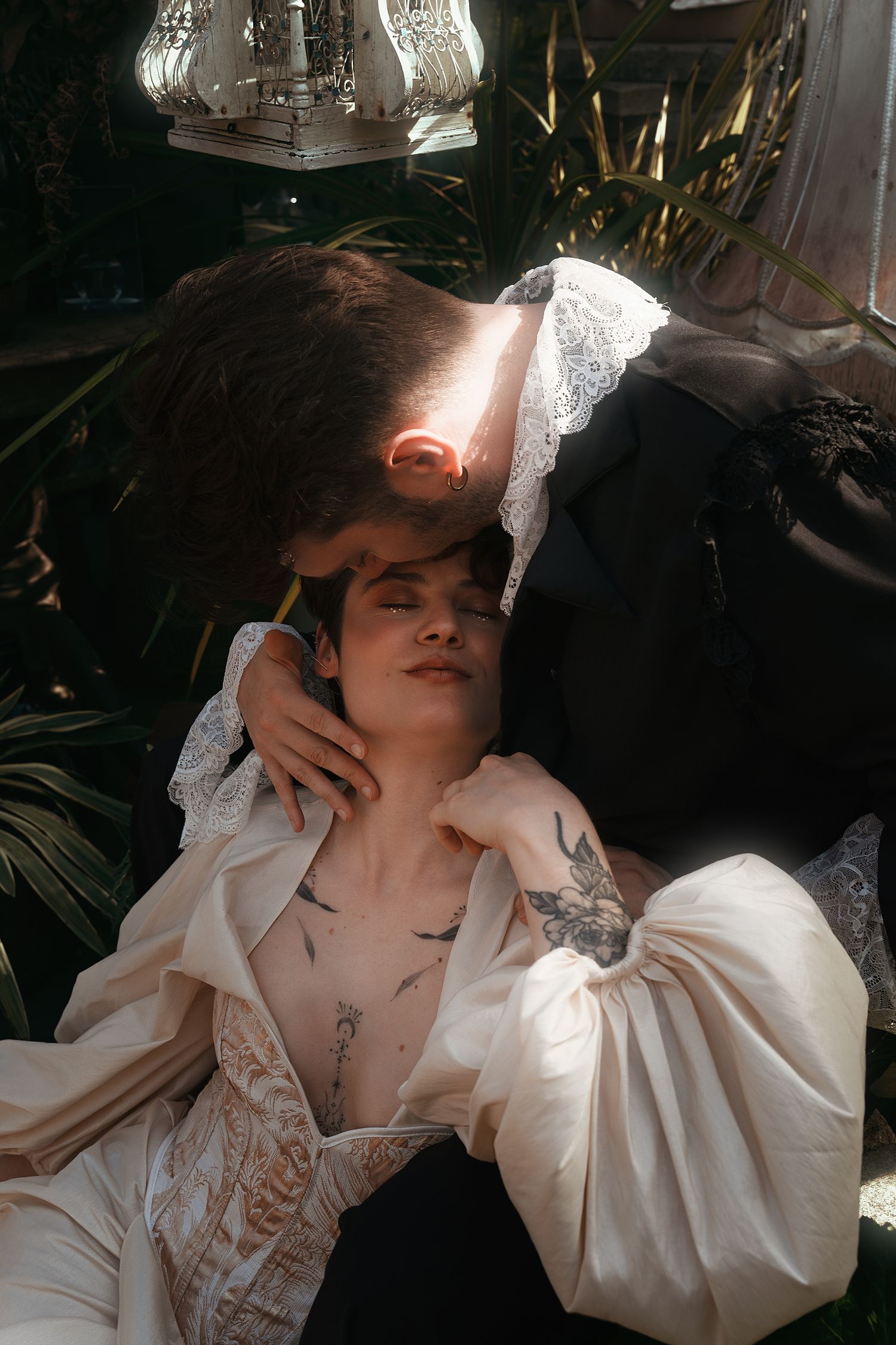 Romantic couple in vintage Victorian attire sharing intimate moment among tropical greenhouse plants.