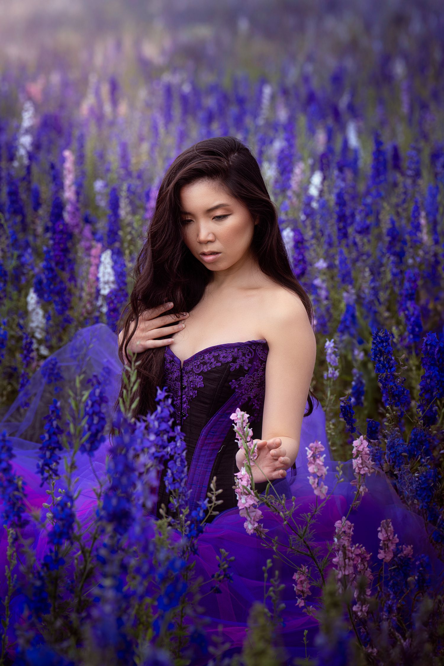 Young woman in purple lace dress standing gracefully among vibrant blue and purple wildflowers in bloom.