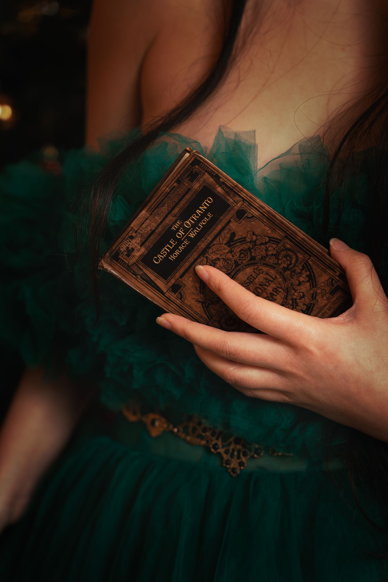 Woman in green tulle gown holding antique book The Castle of Otranto by Horace Walpole.