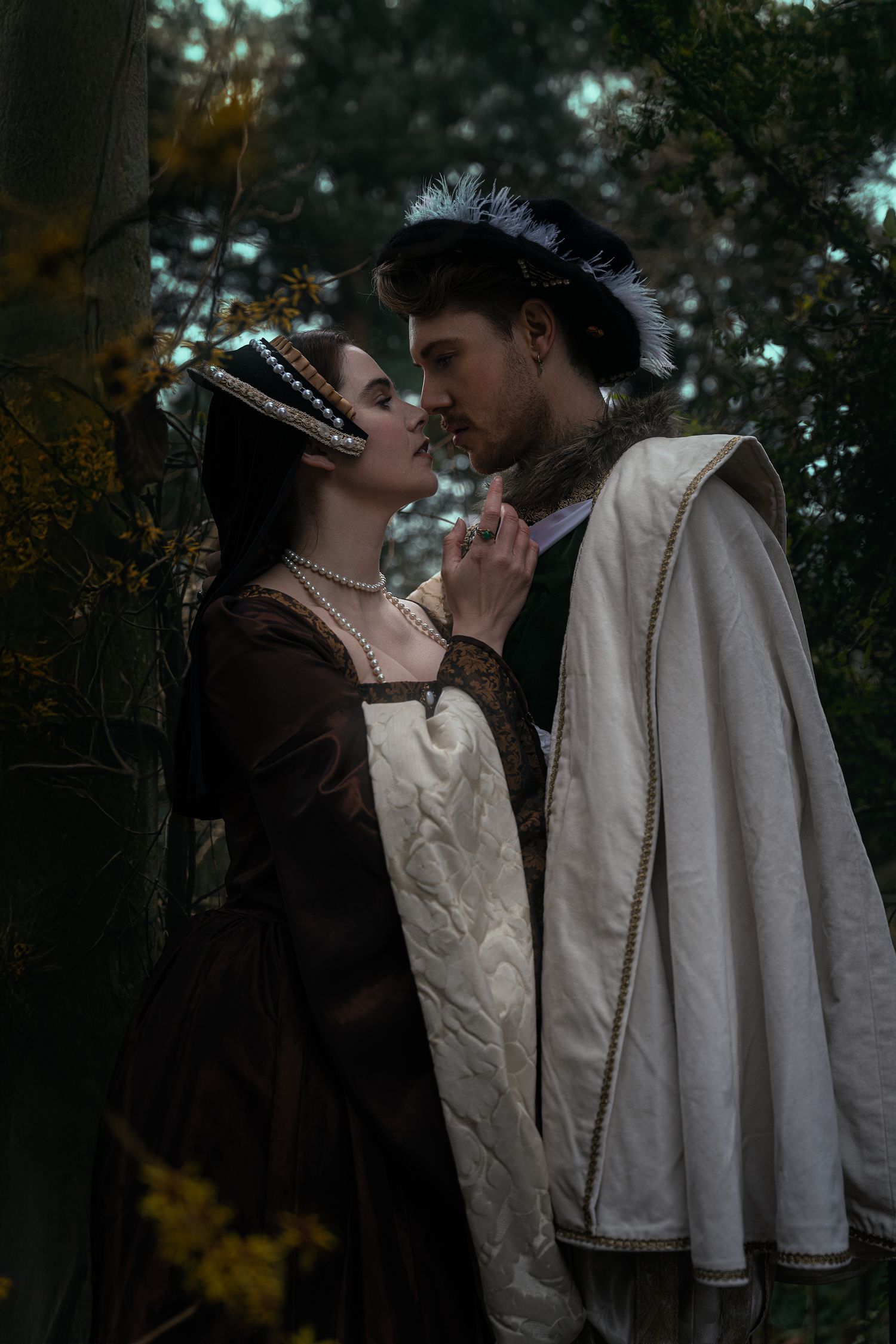 Medieval couple in renaissance costumes sharing a romantic moment in an enchanted forest setting.