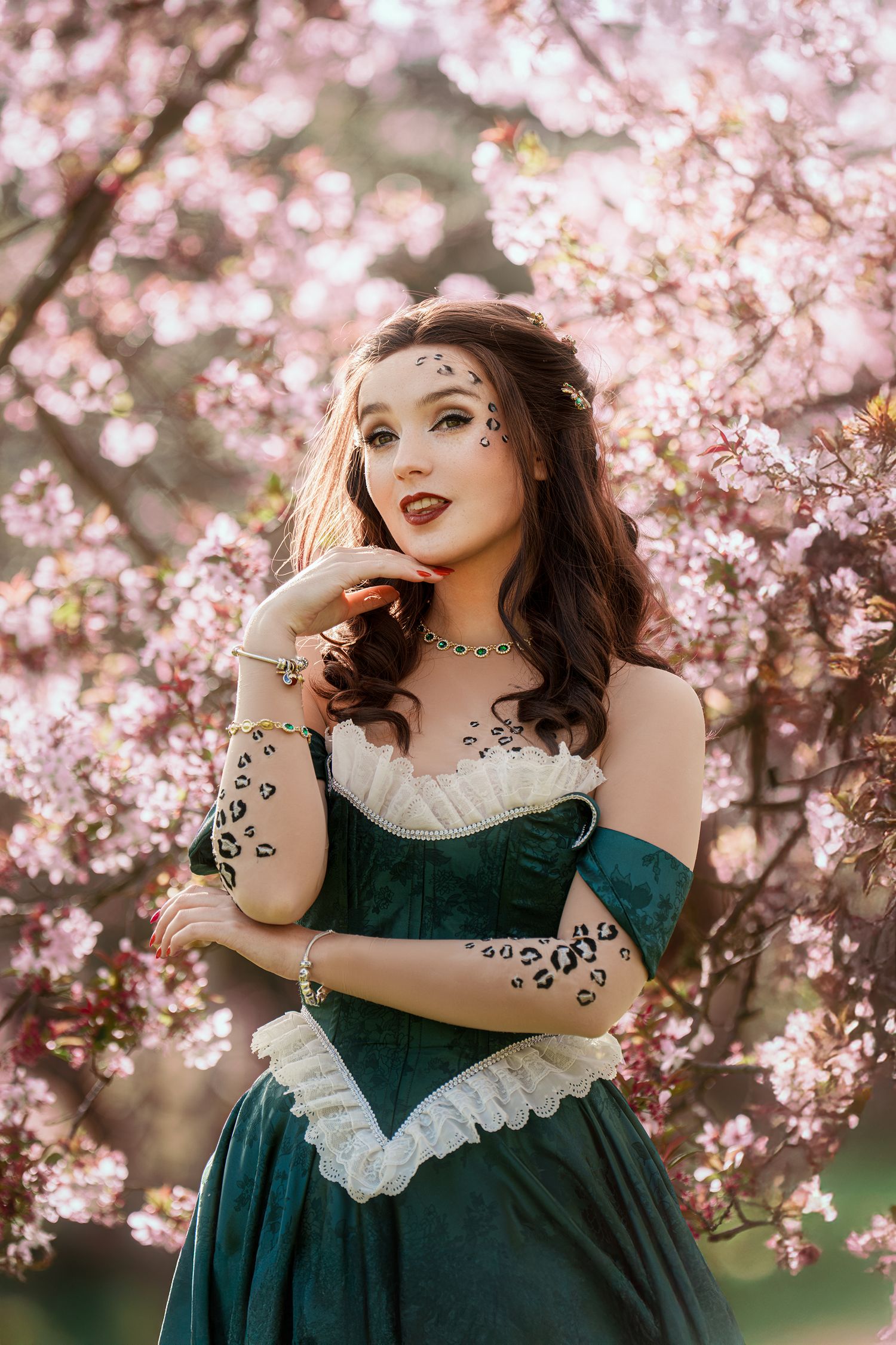 Woman in teal corset dress with leopard print body art near pink cherry blossom tree.