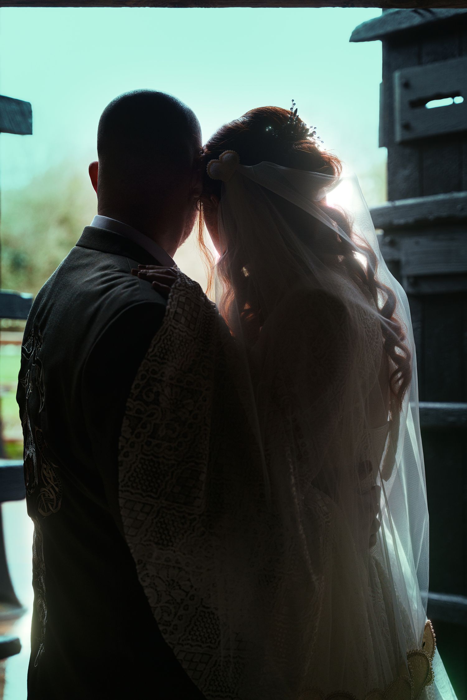 Silhouette of bride and groom standing together in backlit doorway on their wedding day.