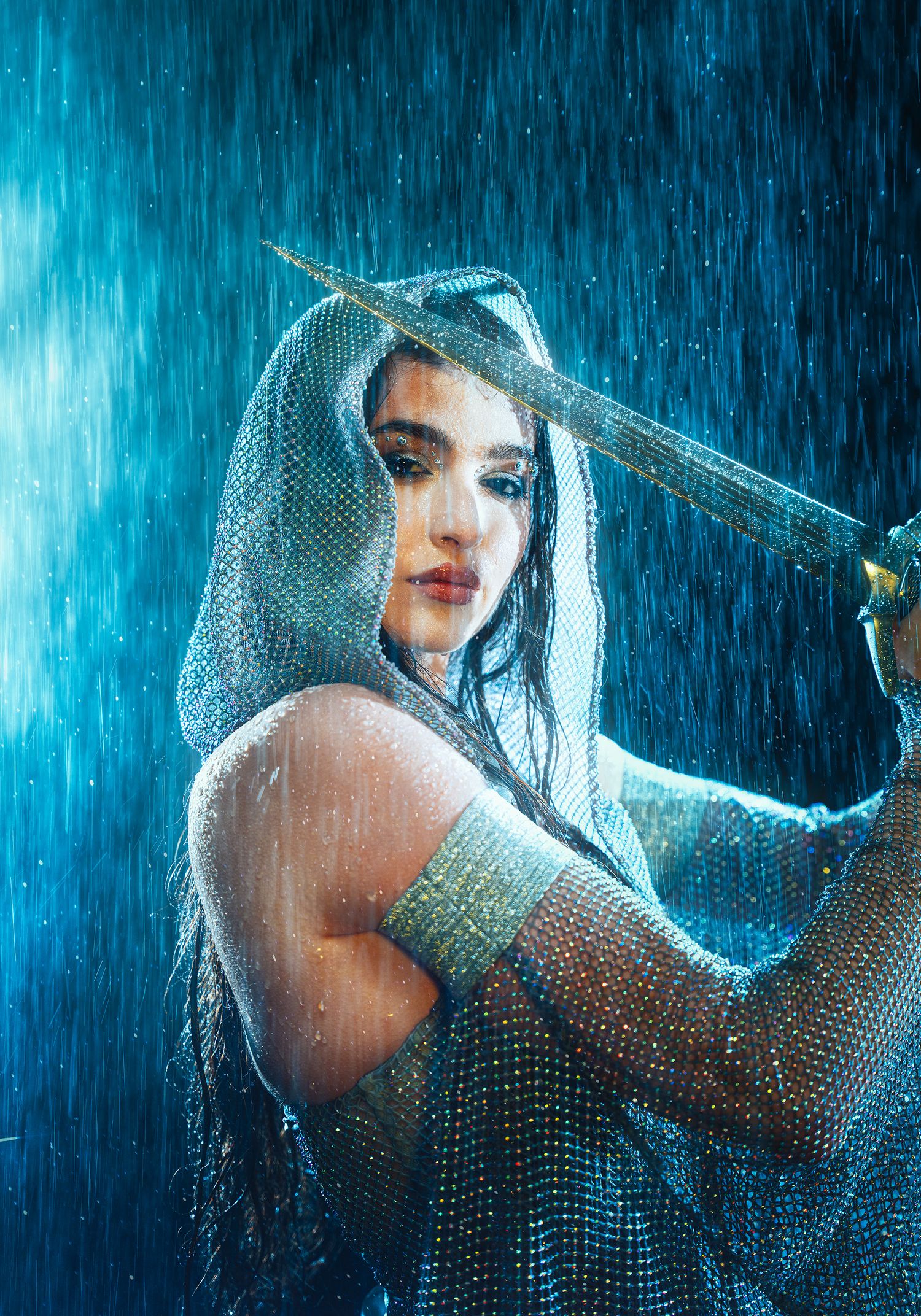 Fierce warrior woman in silver mesh veil wielding sword in blue rain storm.
