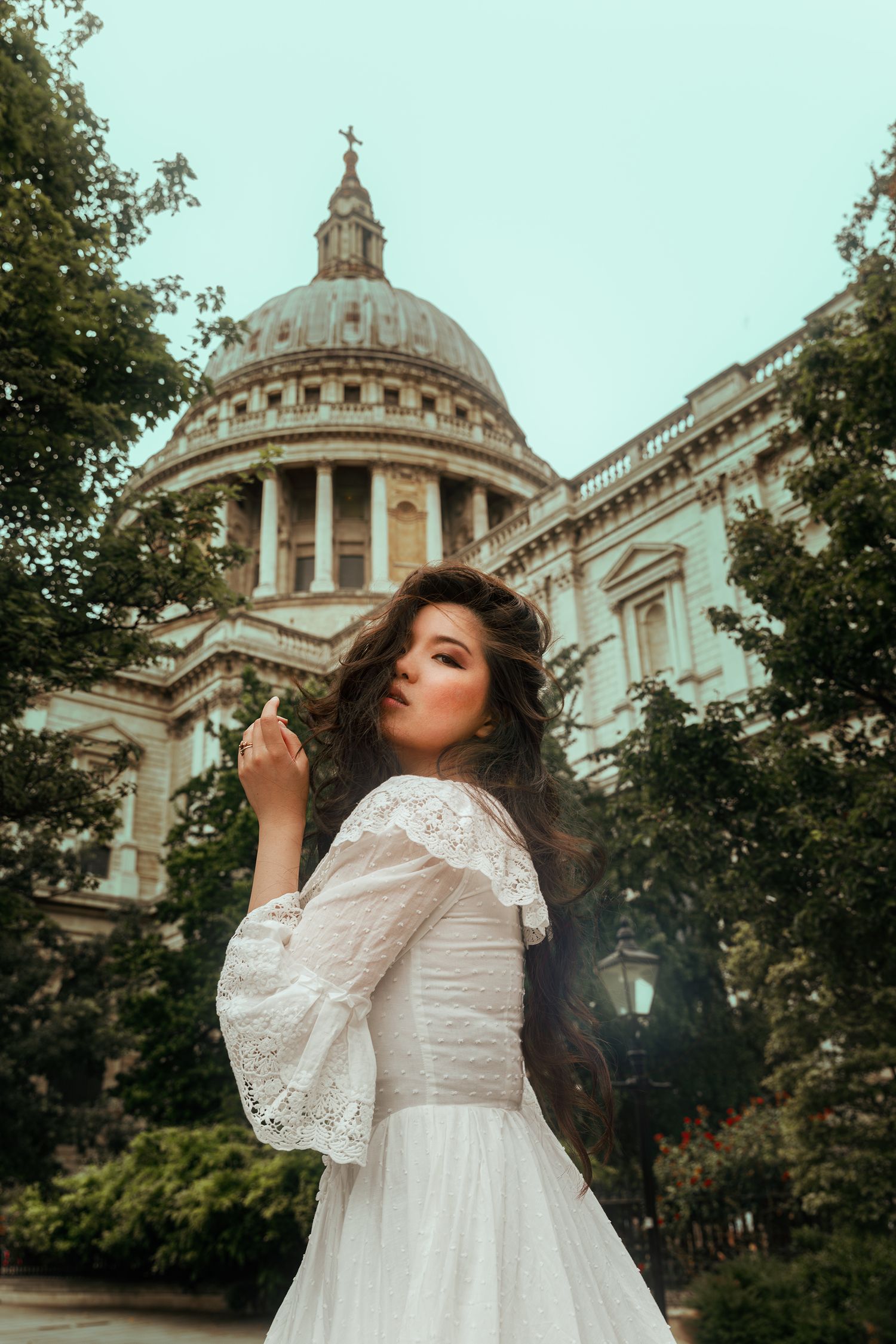 Elegant woman in white lace dress with bell sleeves poses before St Paul's Cathedral in London.