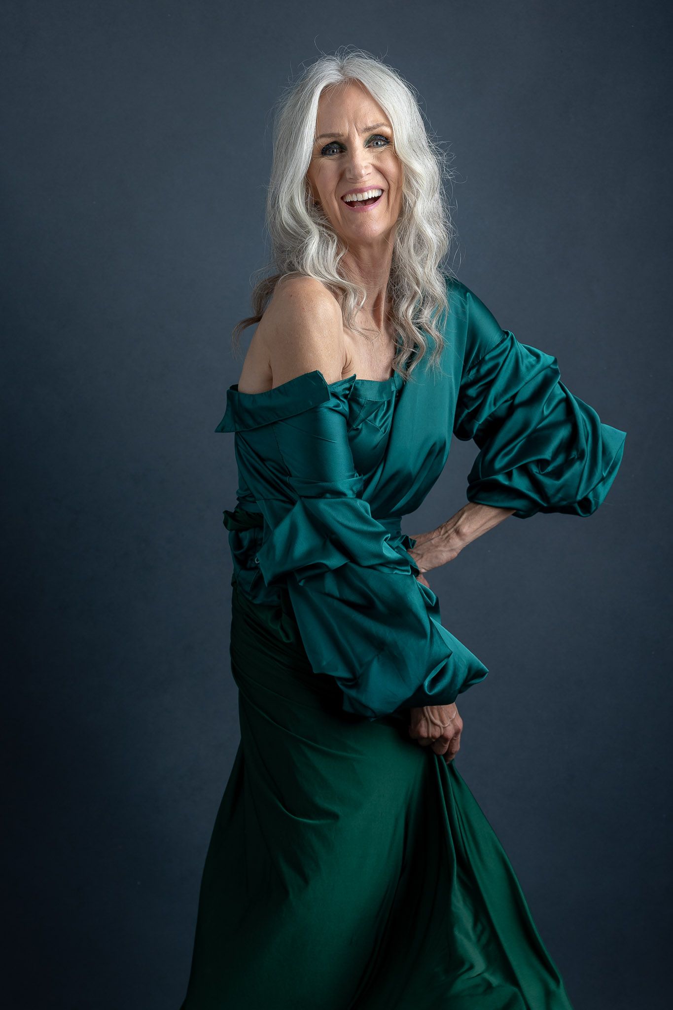 Dynamic fashion poses in emerald green evening gown against dark backdrop.