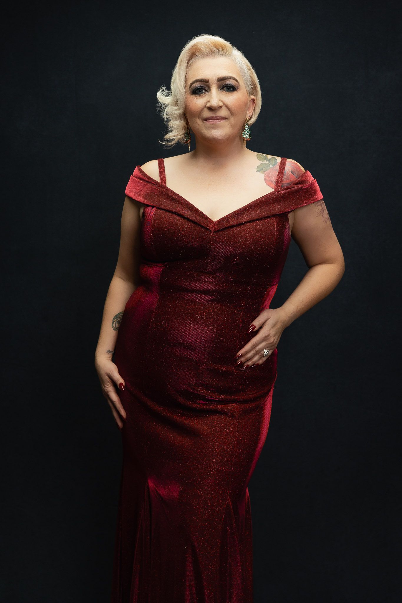 Elegant portraits in deep burgundy evening gown against black backdrop.