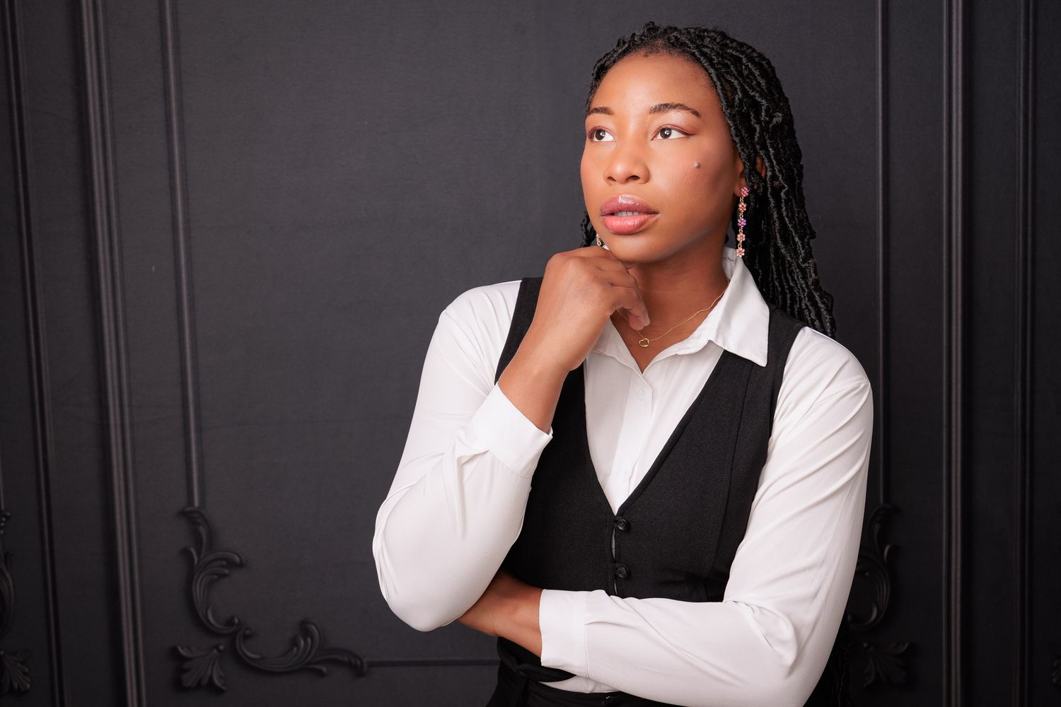 Professional portrait of someone in business attire with a white shirt and black vest against a dark background.