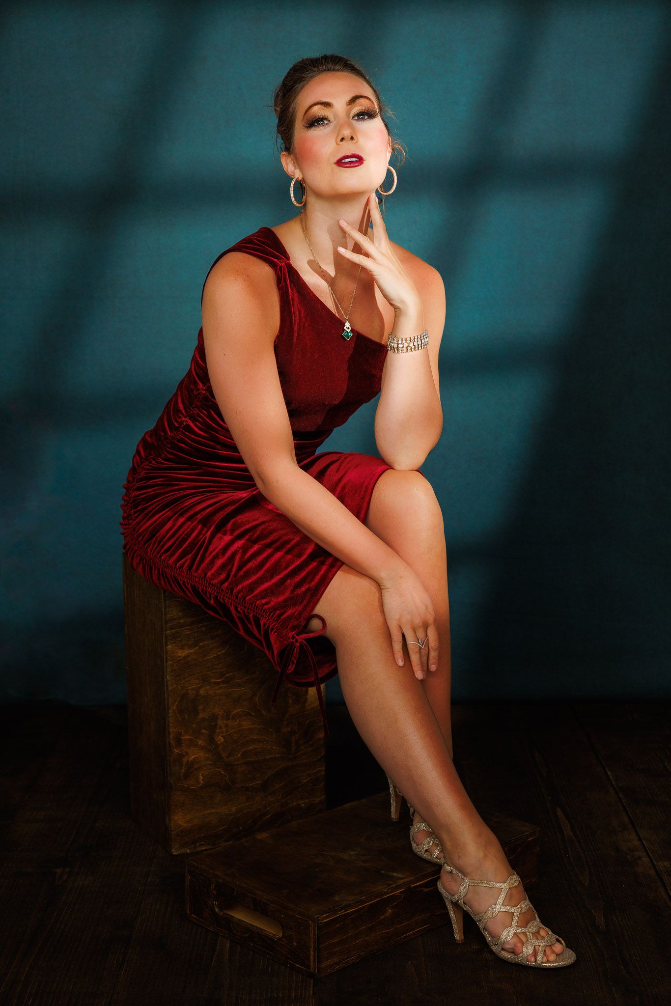 Glamour portrait series in burgundy velvet dress against teal background.
