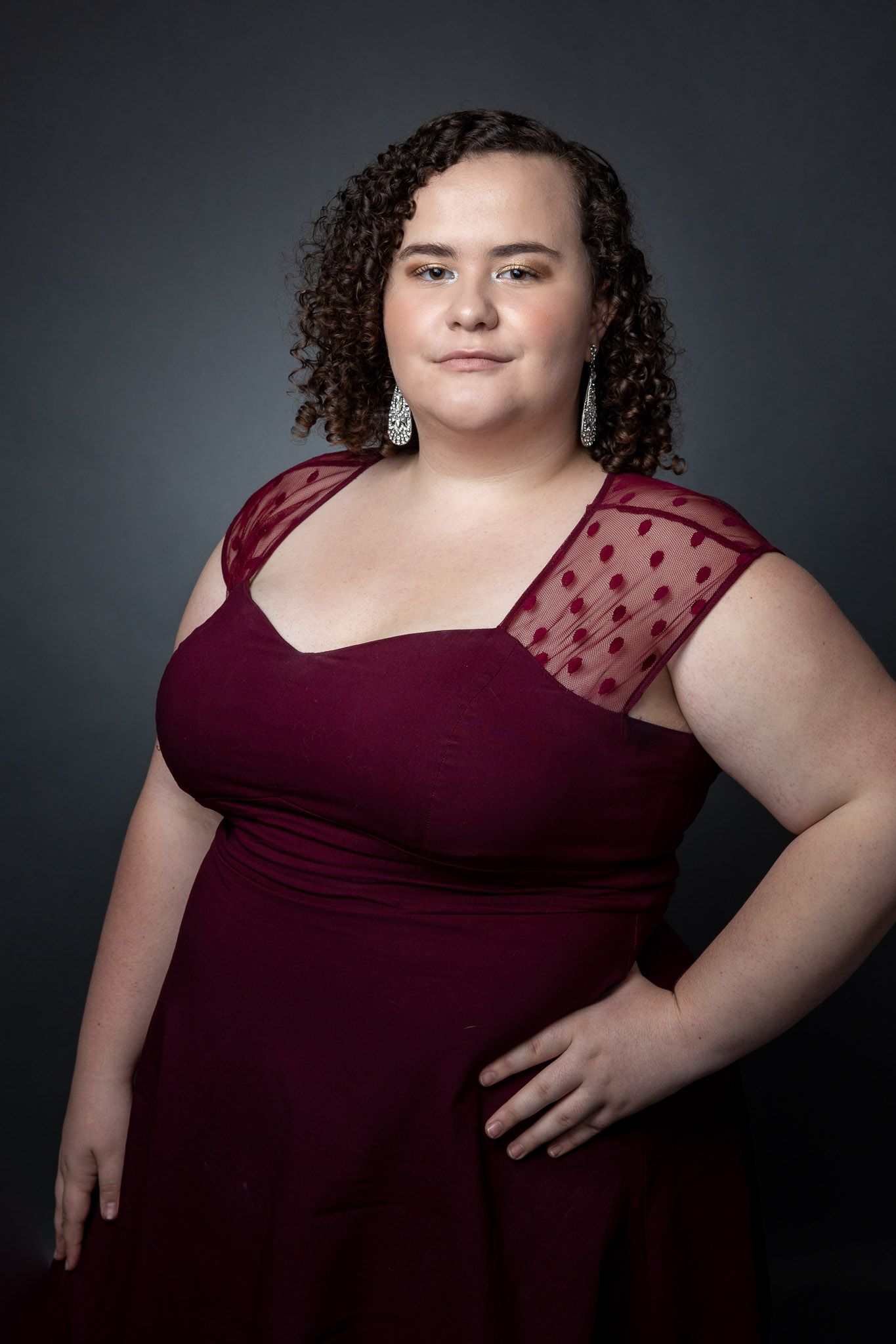 A burgundy dress with sheer polka dot details on the shoulder is showcased in a studio portrait session.