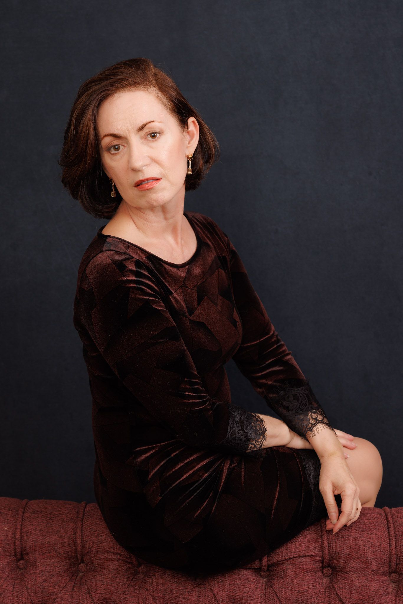 Studio portrait series in brown velvet dress against dark backdrop.