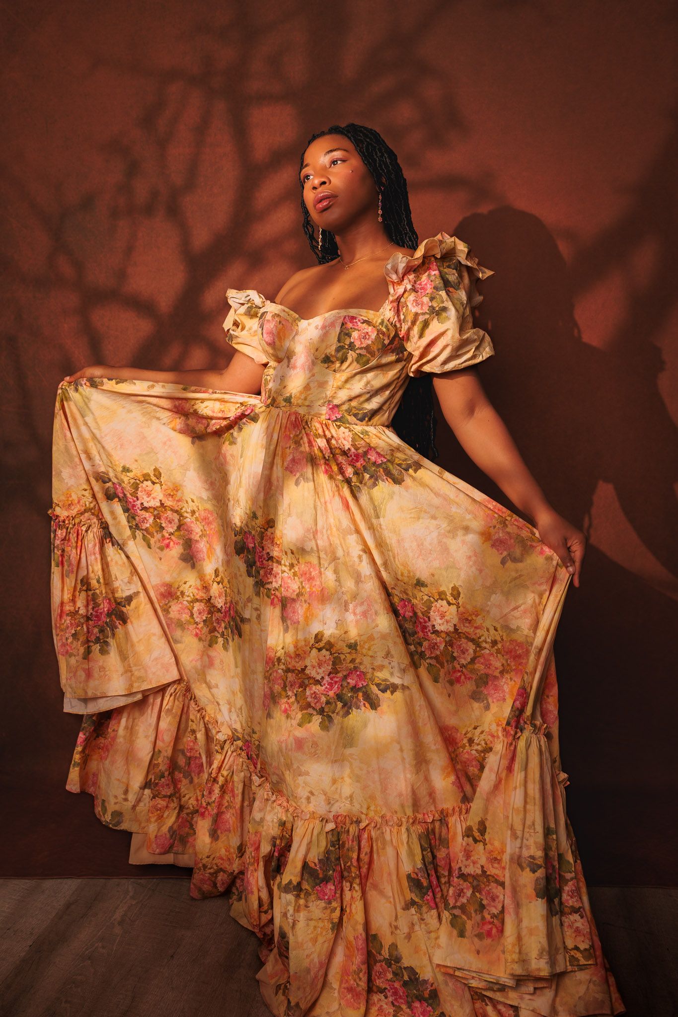 Artistic portrait series showing flowing floral dress against warm red backdrop.
