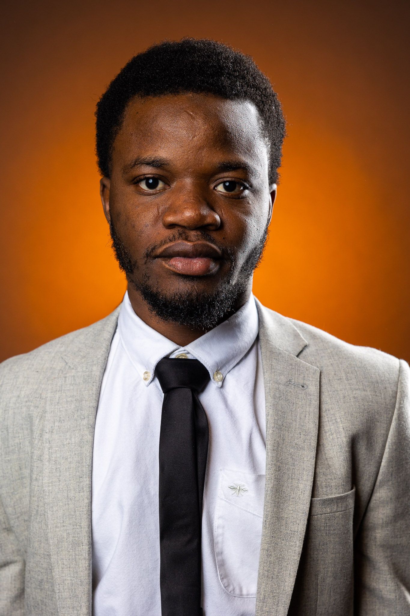 Professional headshot series in grey suit and black tie against orange background.