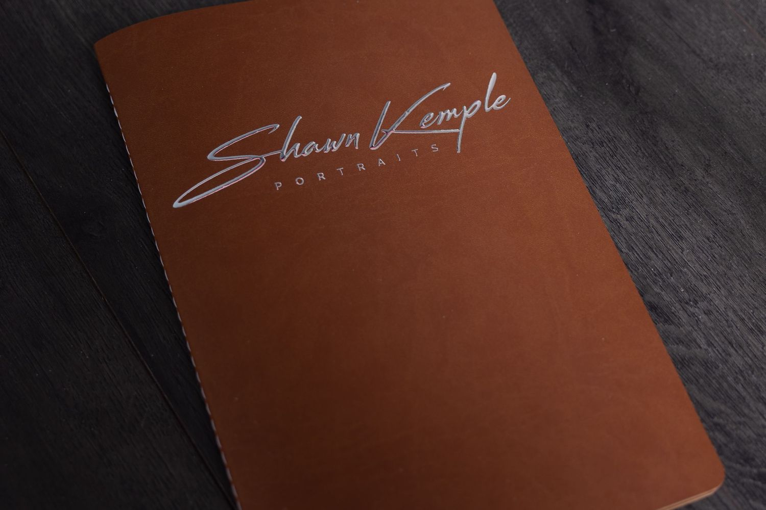 Brown leather portfolio album with elegant signature branding on cover.
