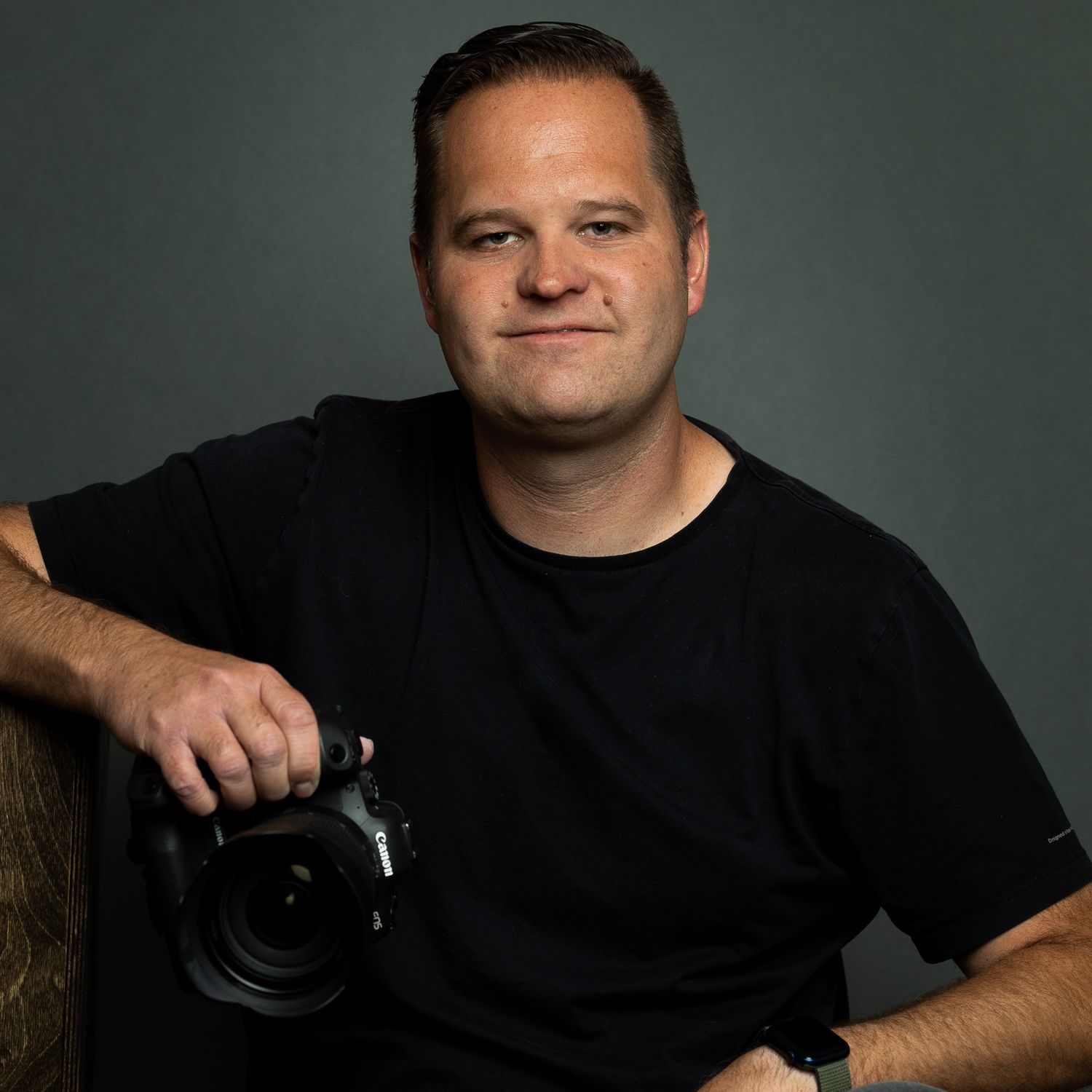 Studio portraits of photographer holding camera against dark background.