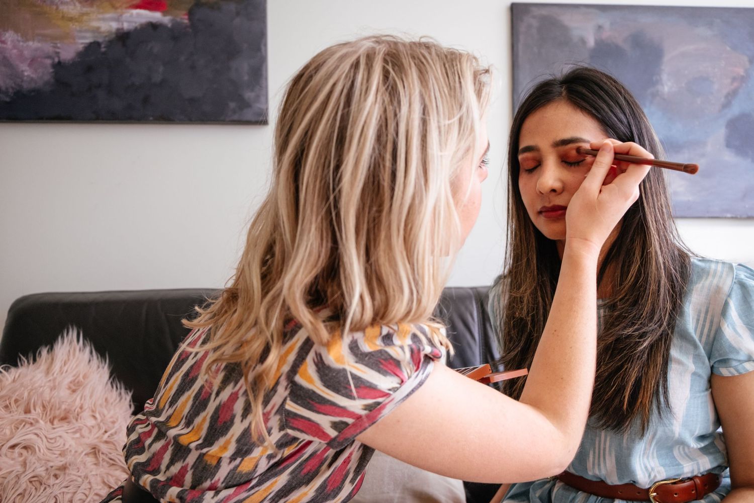 Makeup artist applying cosmetics to a client in a bright home setting.
