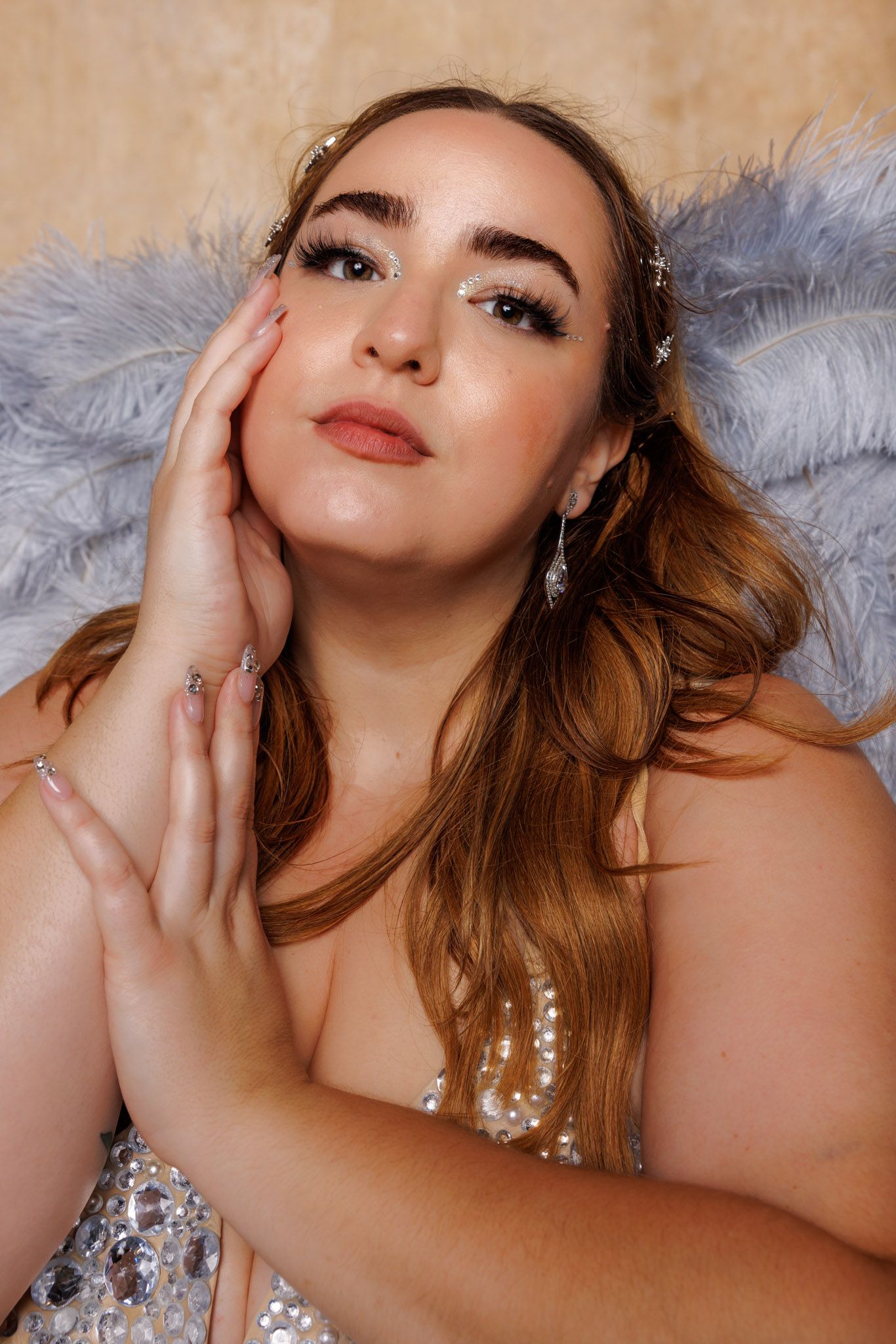 Close up portrait against gray angel wings with soft warm lighting and glamorous makeup and jewelry.