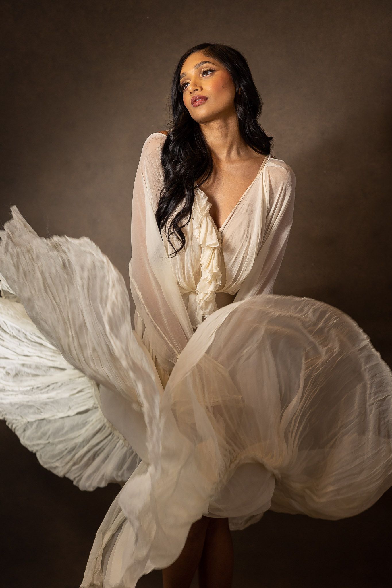 Flowing white fabric creates dramatic movement in an artistic portrait against a dark background.